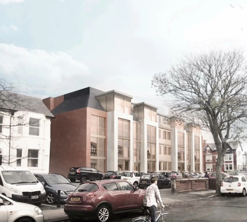 Modern building with large windows behind a parking lot filled with various cars, a man walking with a bicycle, and leafless trees in the foreground.