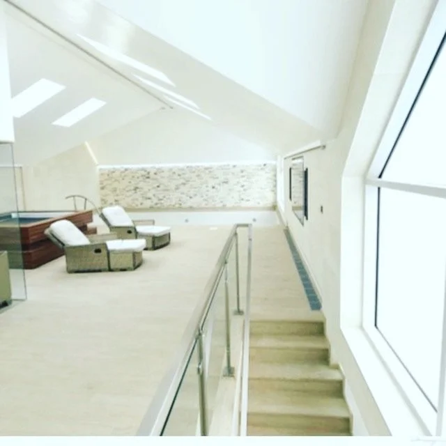 A bright, modern interior with a sloped ceiling, large windows, and seating area with wicker chairs and throw pillows.