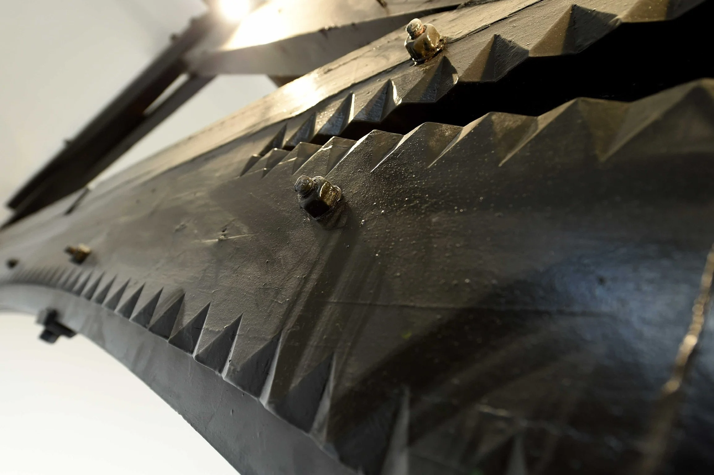 Close-up of a large, black metal machine part with sharp, jagged teeth and bolts.
