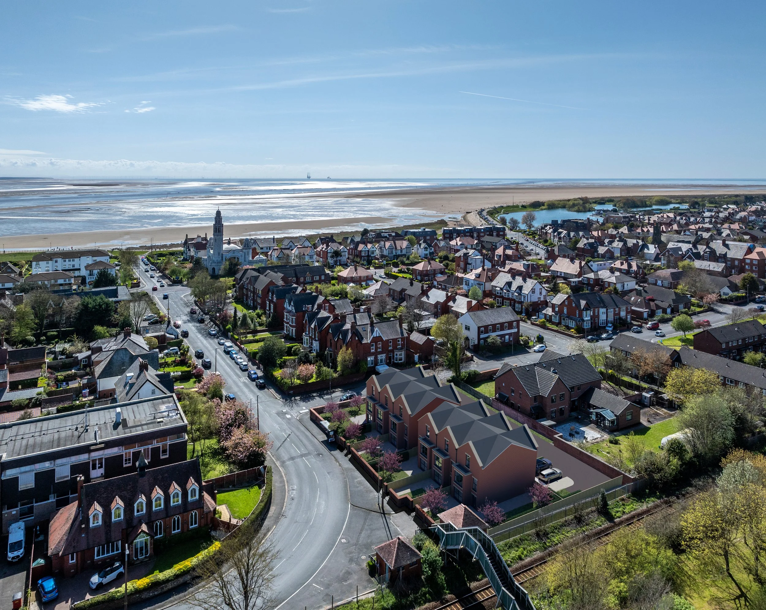 Aerial view of a coastal town with houses, streets, and a church, overlooking an ocean beach under a clear blue sky.