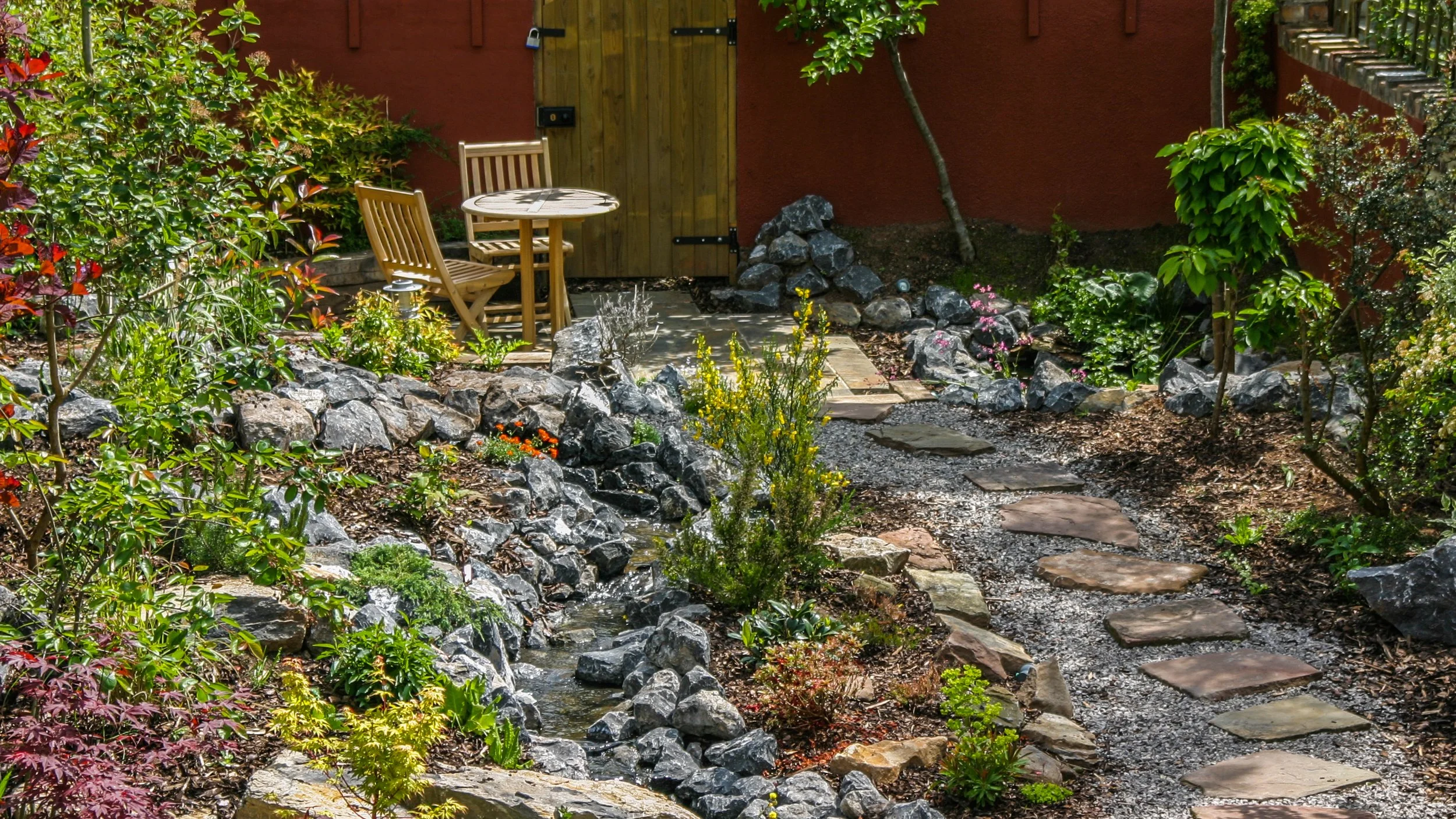 Stream and rockery with stepping stones and Bistro set on a patio at the back