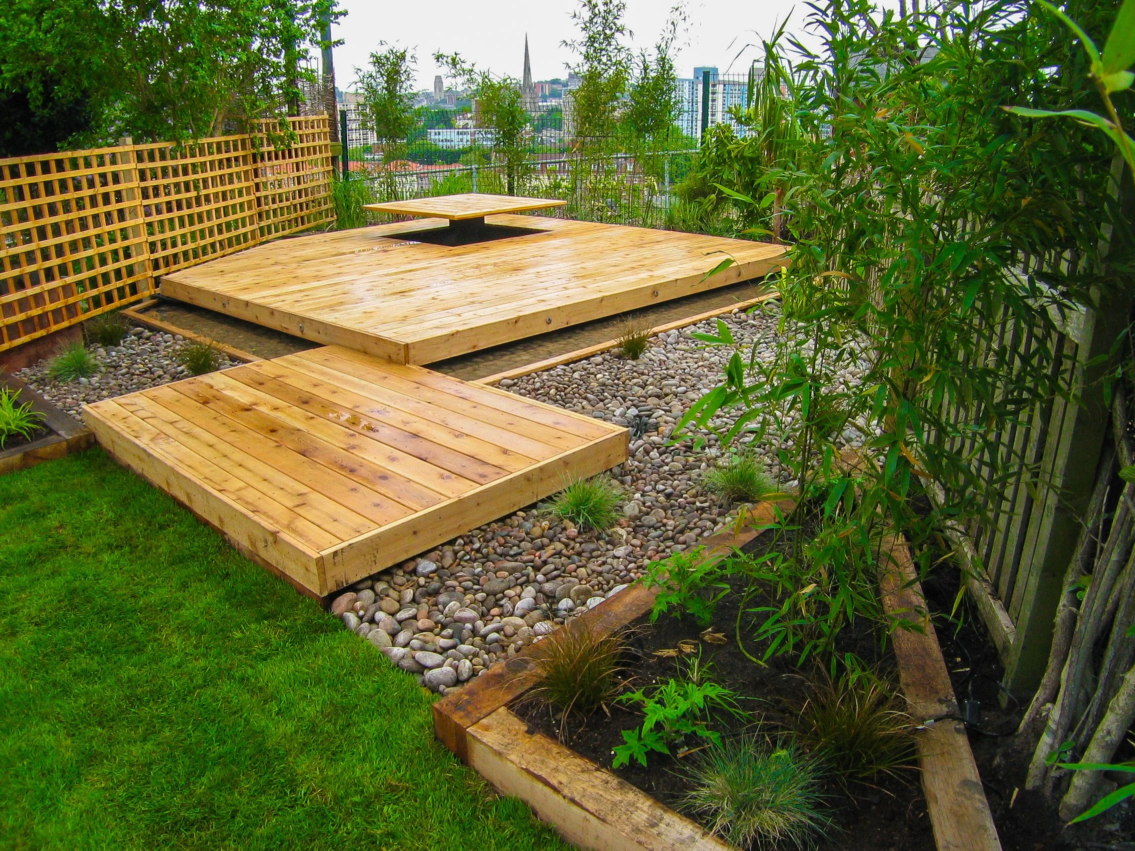 Image of a lush green lawn and light timber, raised decking.   View over a city