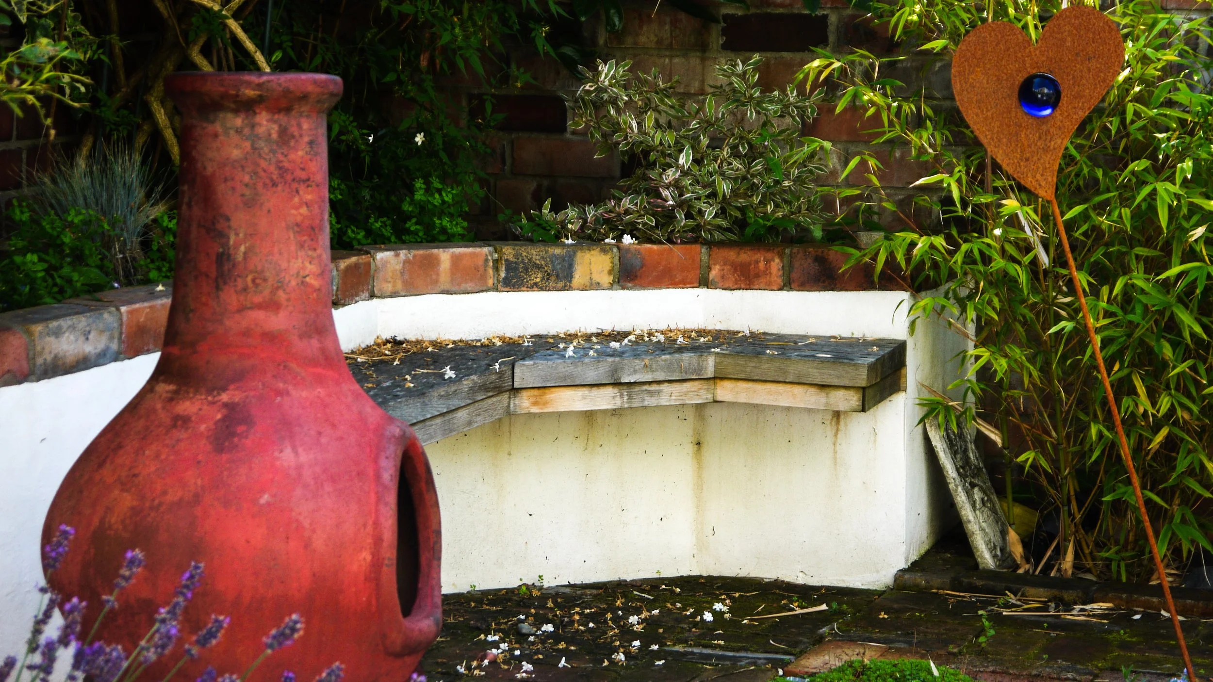 An image of the eco garden.  small bench on wall, BBQ and corten steel heart sculpture