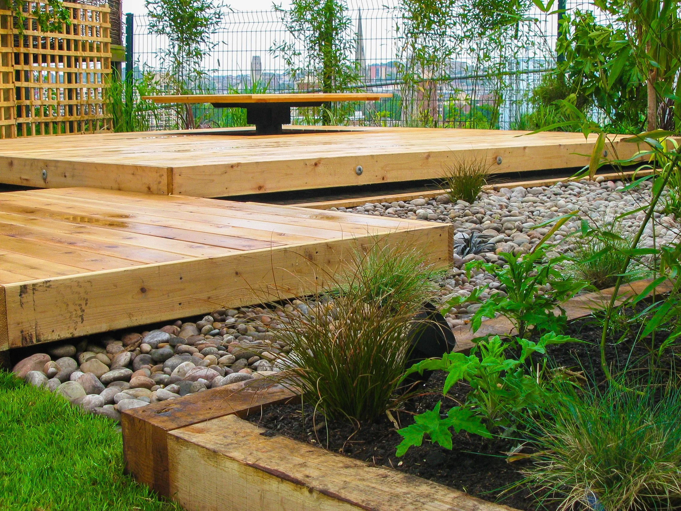 Image of planting and light timber, raised decking.   View over a city