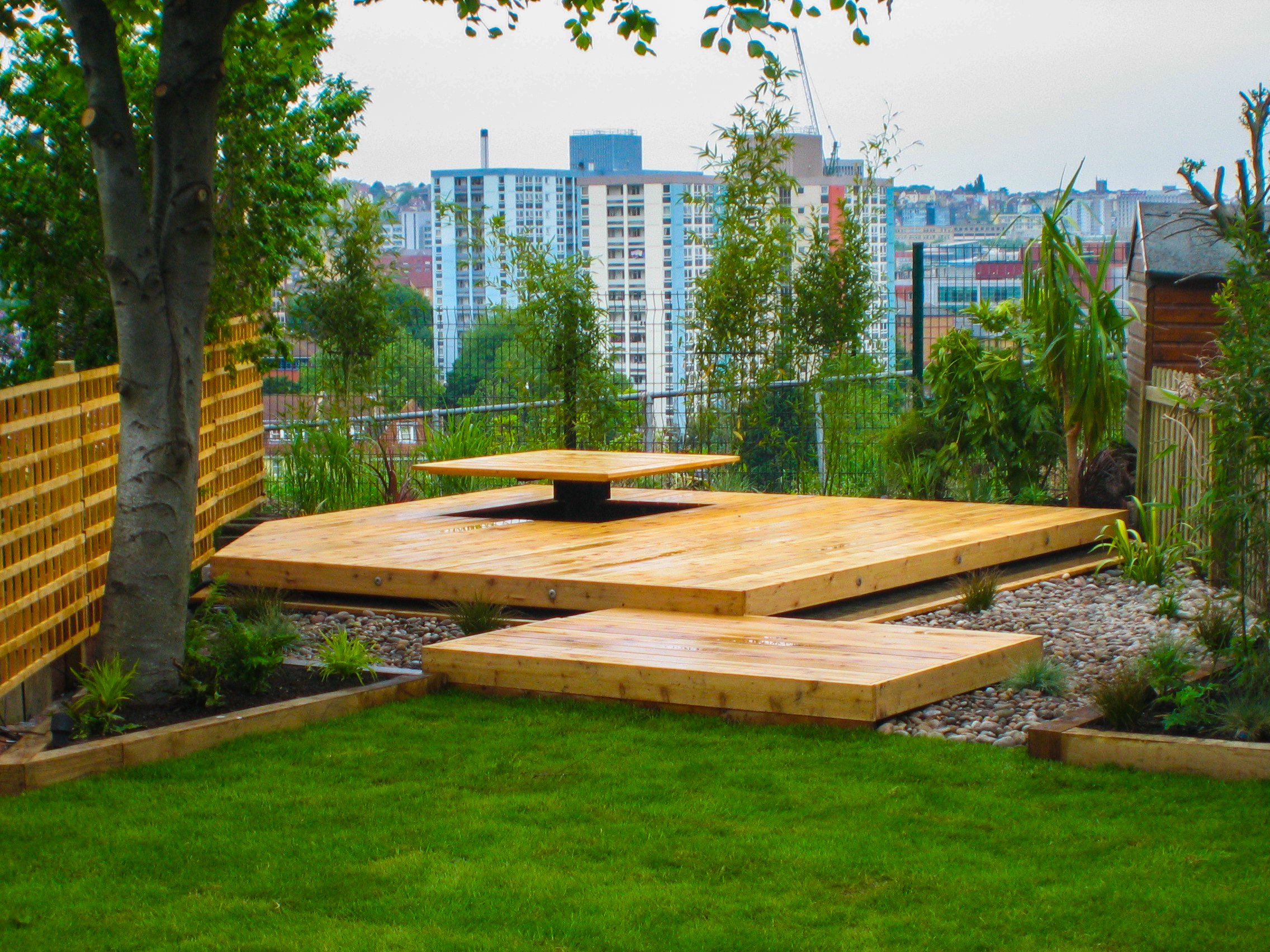 Image of a lush green lawn and light timber, raised decking.   View over a city