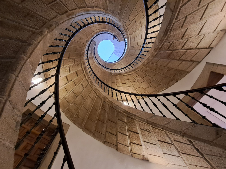 Spiral staircase looking upward toward a circular opening at the top with natural light.