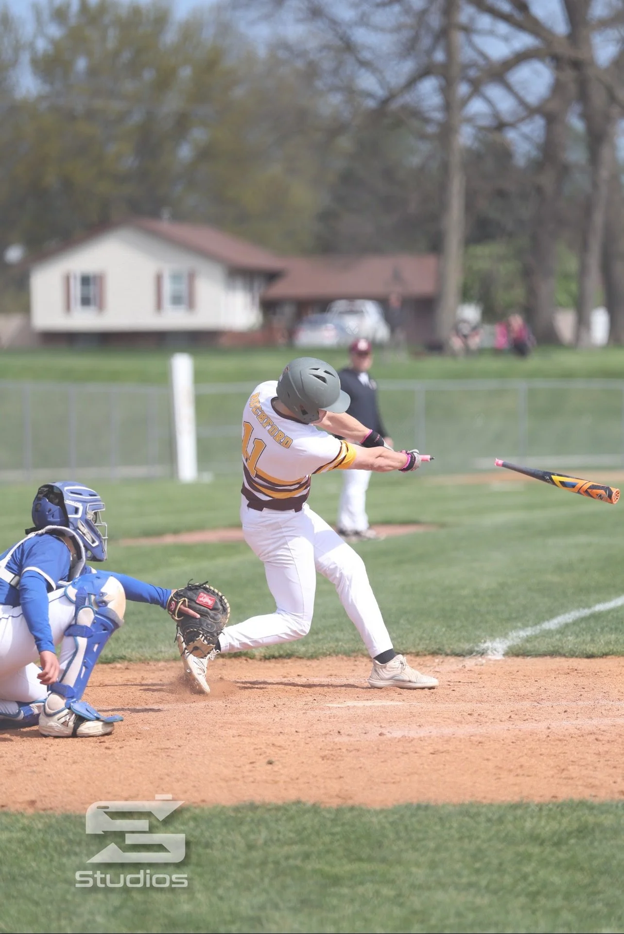 A baseball player sliding into home plate while a catcher from the opposing team attempts to tag him out during a game on a grassy field with houses and trees in the background.