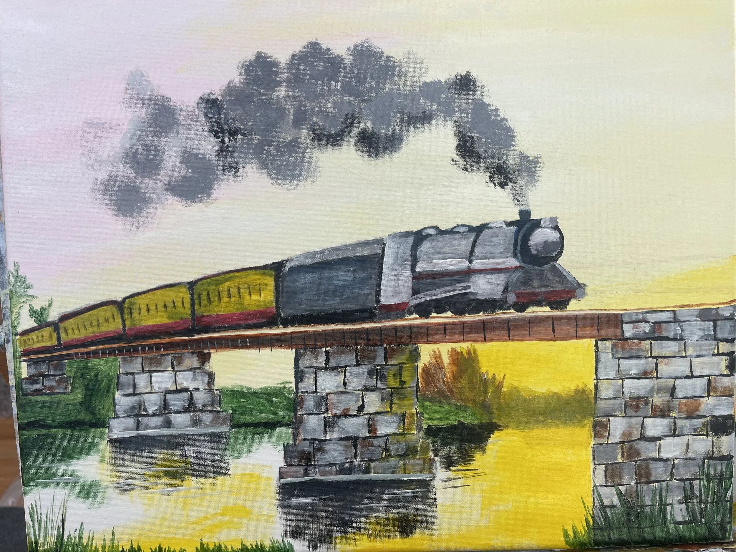 A painting of a steam train with yellow and red cars crossing a stone bridge over a river, with smoke billowing from the engine and a sunset sky in the background.