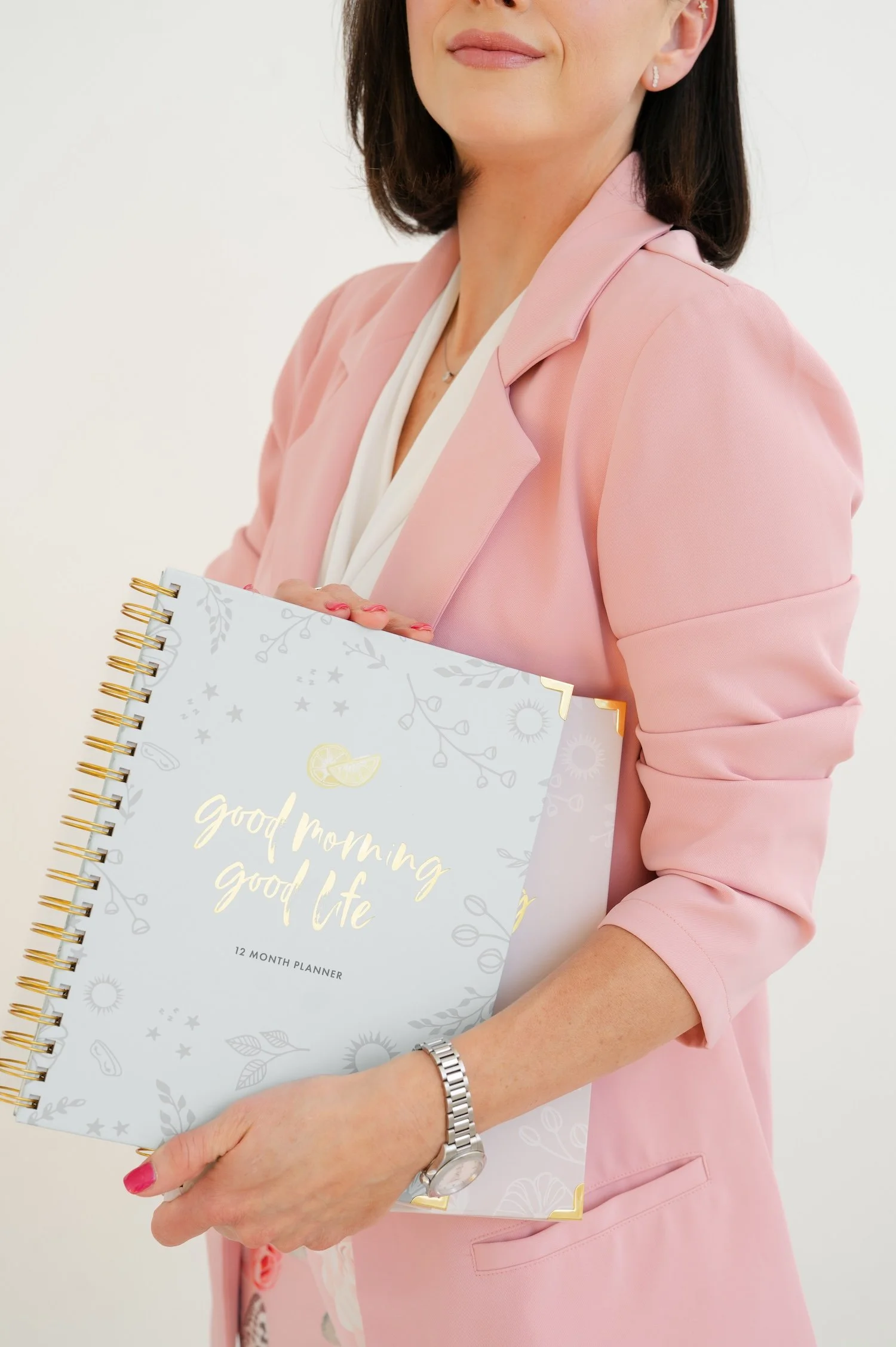 A close up of Amy Landino, author of Good Morning, Good Life, as she holds two of her Good Morning, Good Life Planners. She is wearing a pink blazer.