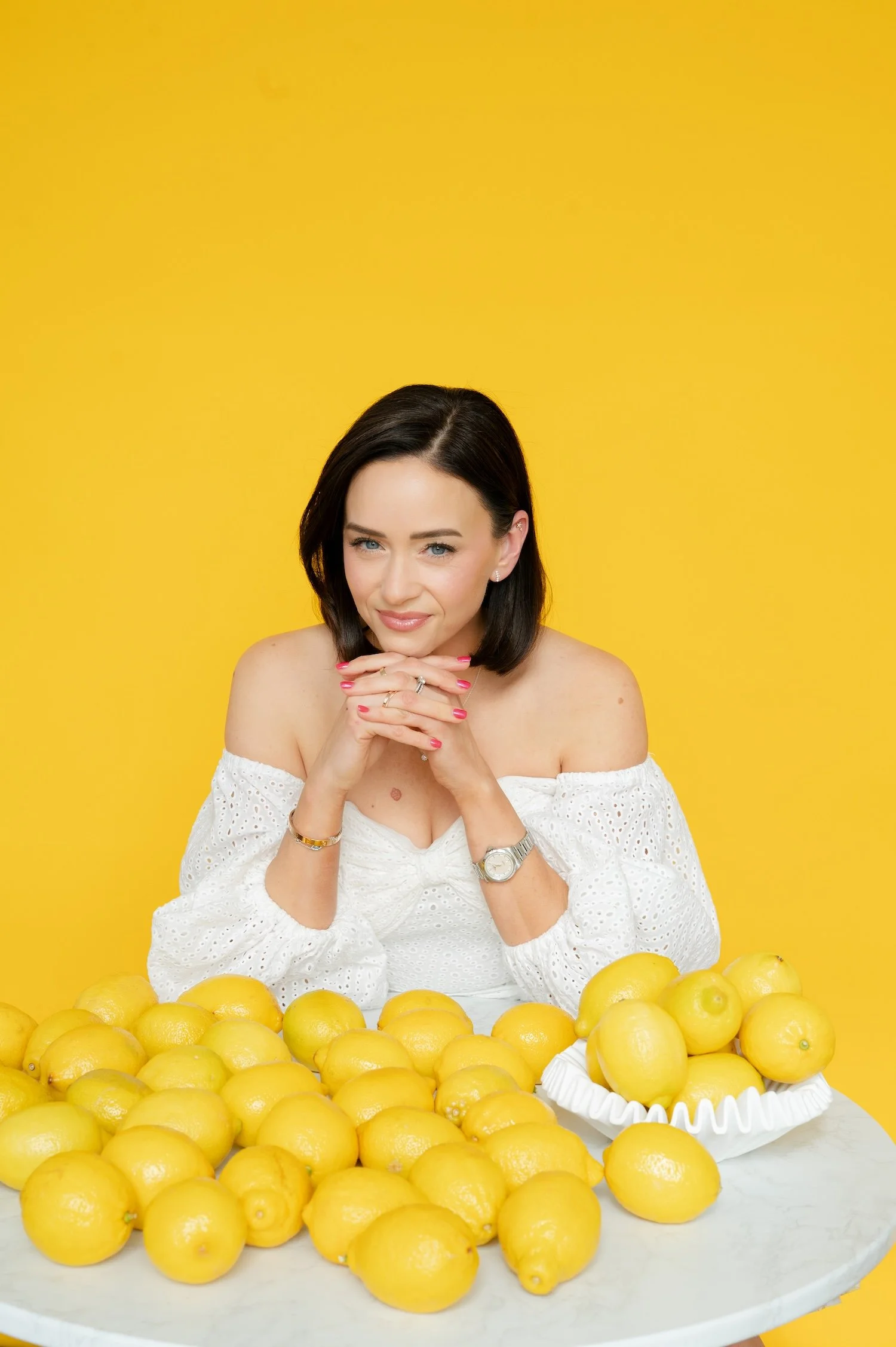 Amy Schmittauer Landino, author of Good Morning, Good Life, sits at a table covered with lemons. She's wearing a white blouse and smiles gently at the camera.