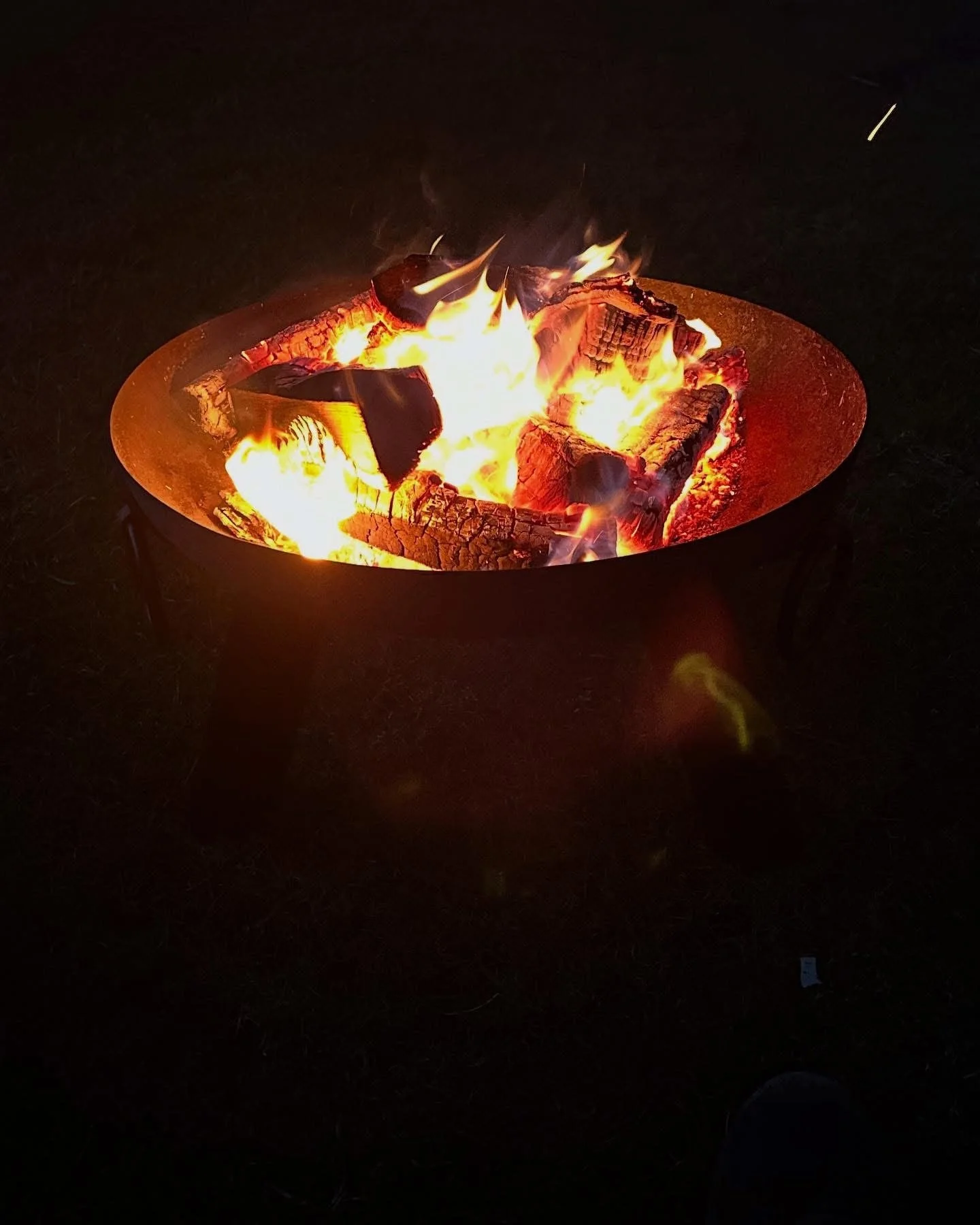 Fire pit with burning logs and flames in a dark outdoor setting.