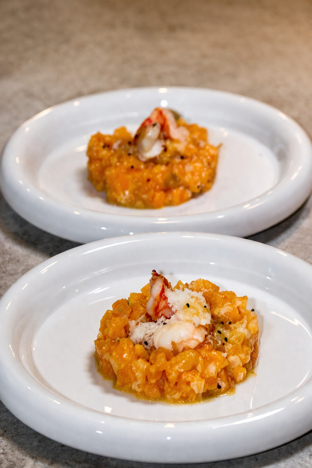Deux assiettes blanches contenant un plat de riz ou de fruits de mer avec des morceaux de crustacés, présentées sur un plan de travail en cuisine.
