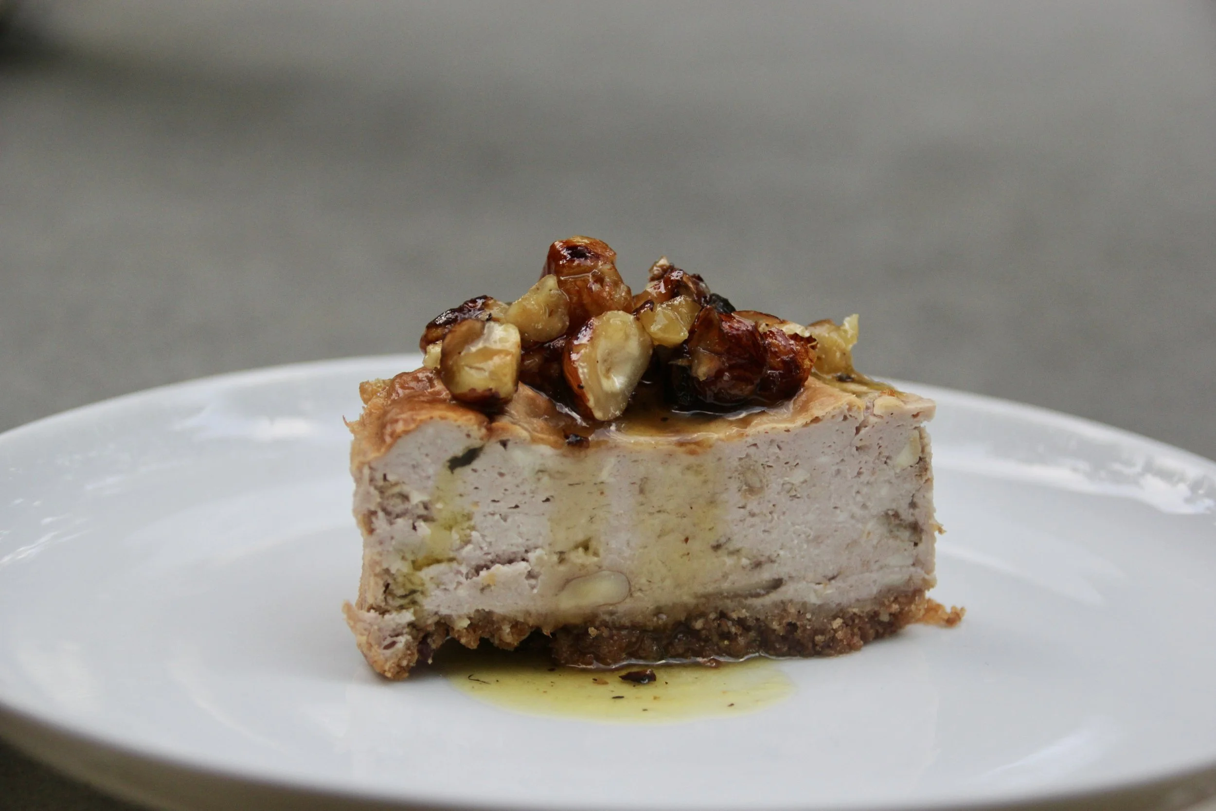 Une tranche de cheesecake garnie de noix et de miel sur une assiette blanche.