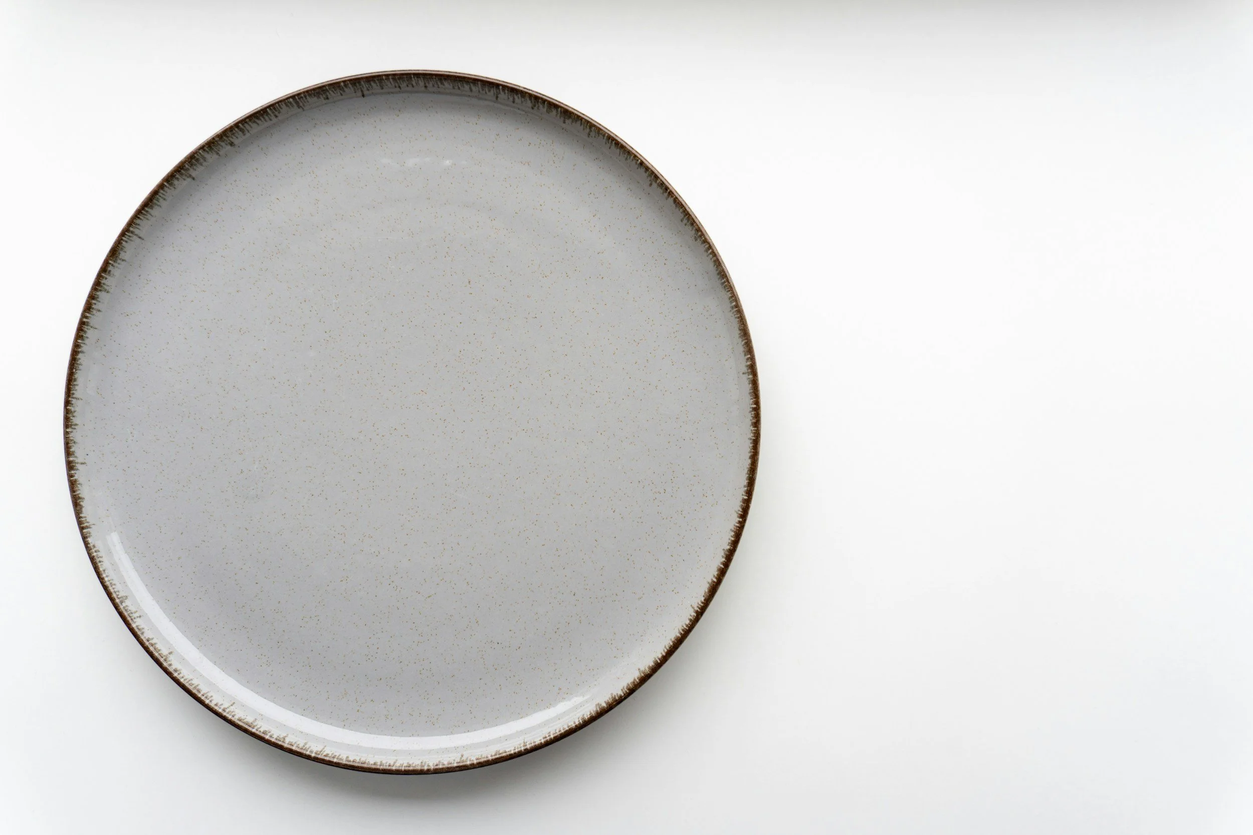 Assiette ronde en céramique blanche avec une bordure brune, vue de dessus, sur fond blanc.