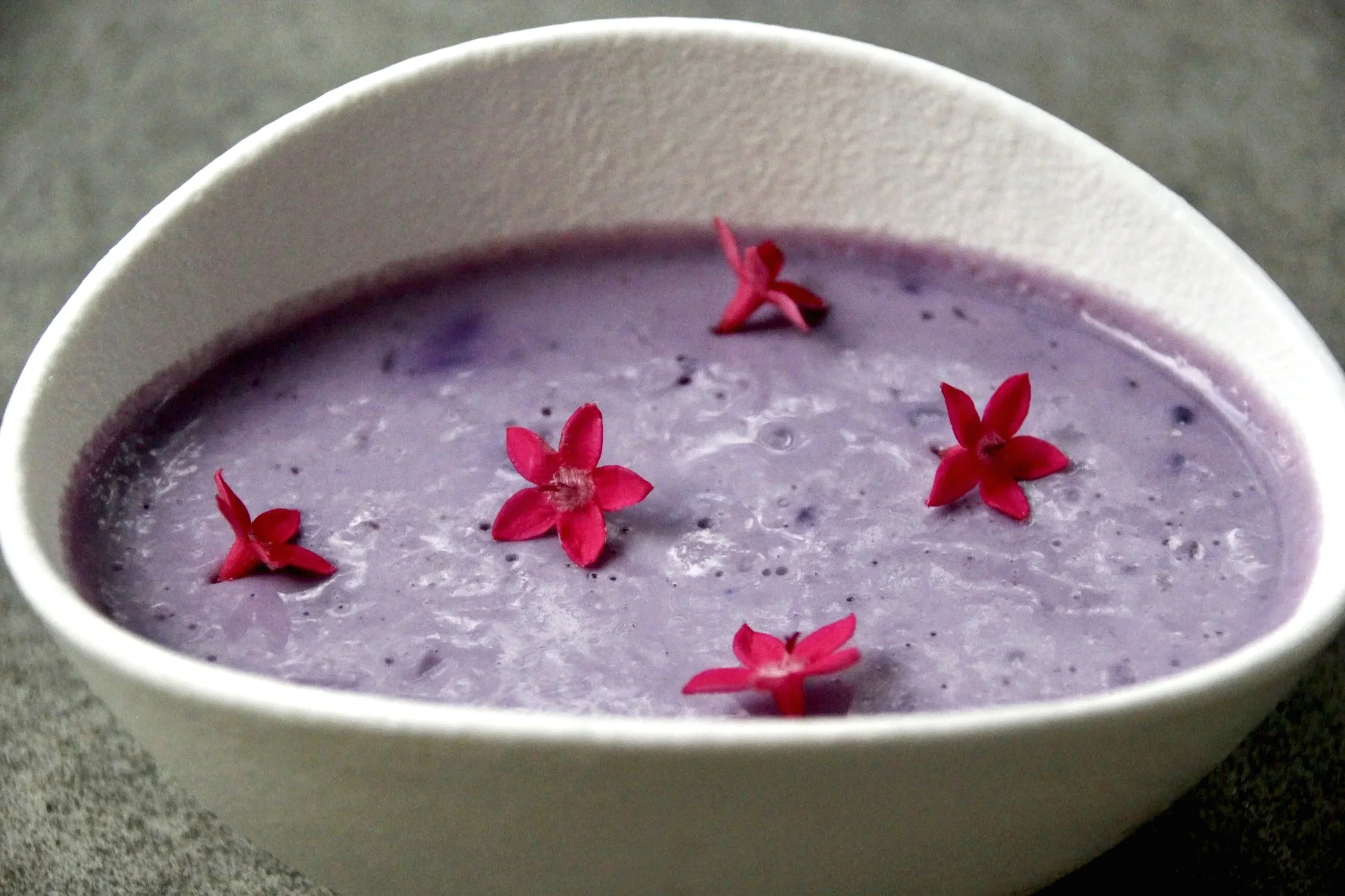 Soupe violette dans un bol blanc avec des fleurs rouges en décoration