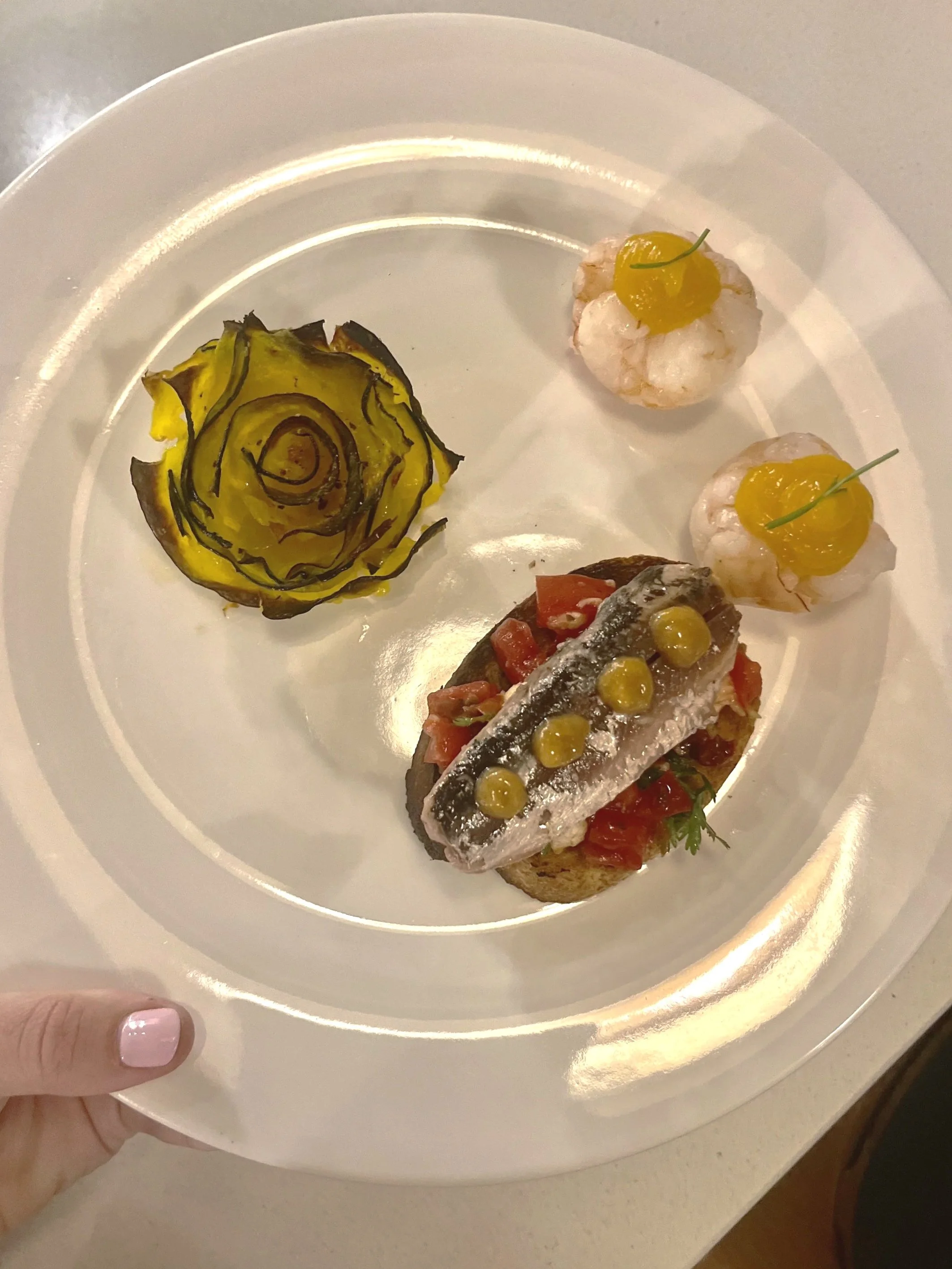 Assiette avec un filet de poisson, double guirlande onctueuse, deux bouchées de légumes de forme ronde, et une tranche de courgette en forme de rose.