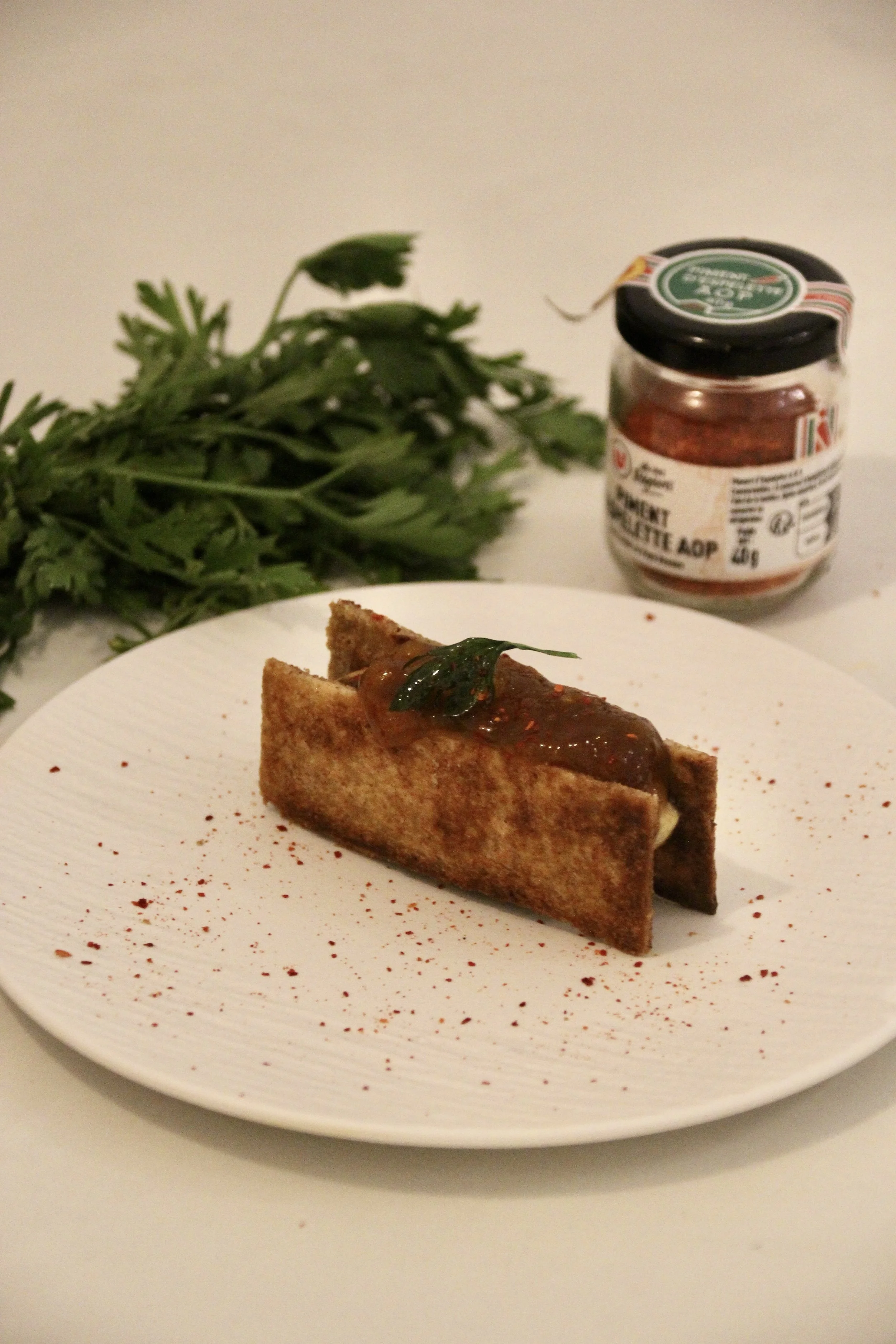 Une assiette avec un taco pourvu de garnitures, surmonté d'une feuille verte et de sauce. En arrière-plan, un bouquet de persil et un pot de sauce piquante.