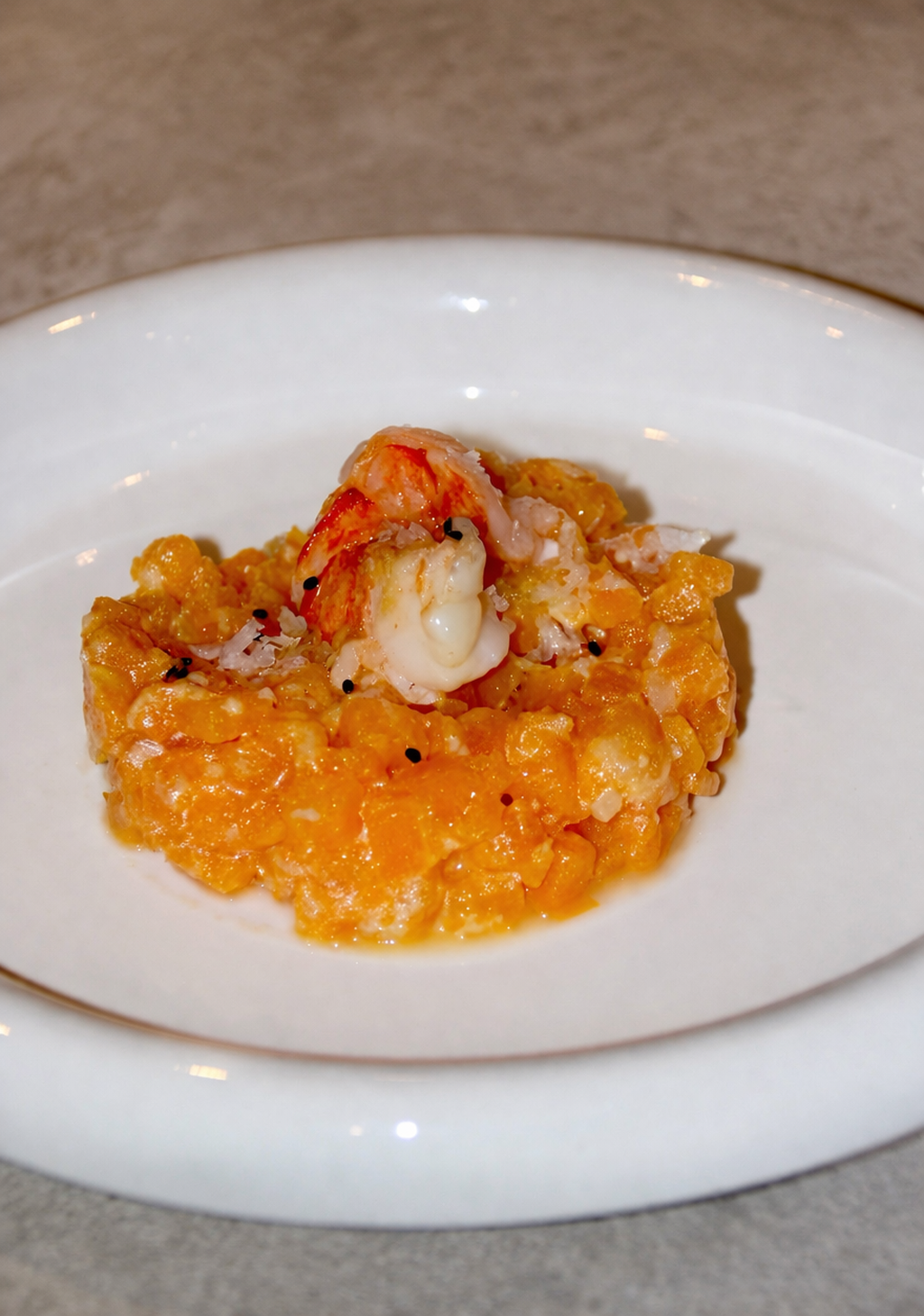 Assiette avec une portion de risotto à la carotte, garnie de crevettes et de parmesan râpé.