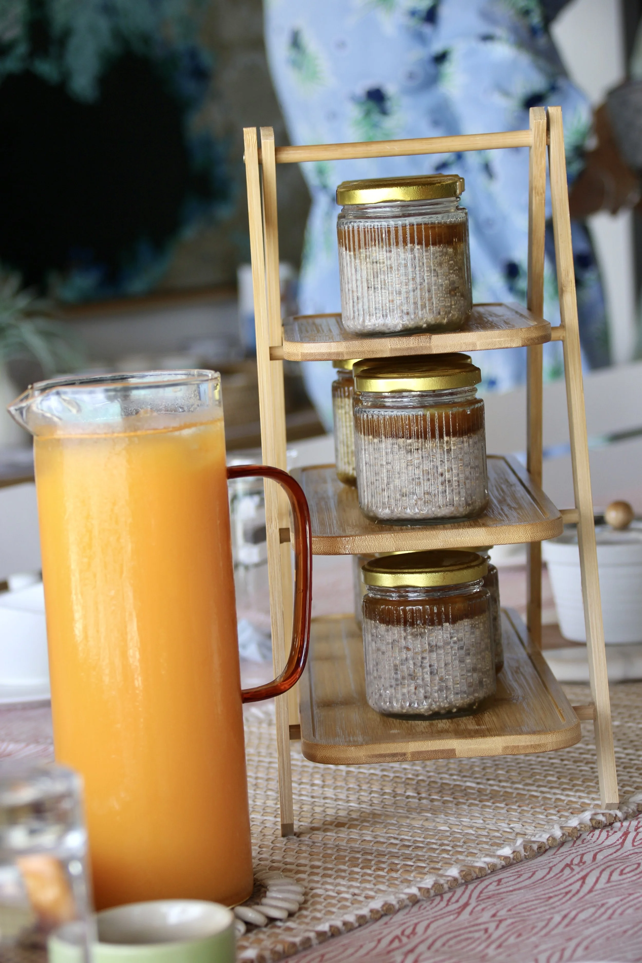 Une carafe de jus d'orange et un plateau en bois avec des bocaux contenant une substance brune, disposés sur une table.