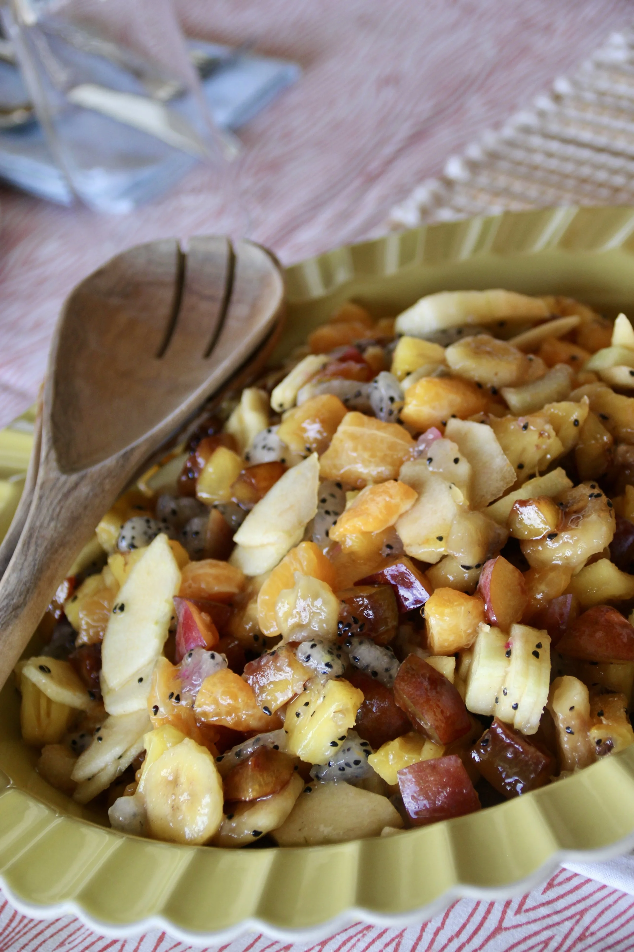 Salade de fruits dans un plat vert avec une cuillère en bois à côté.