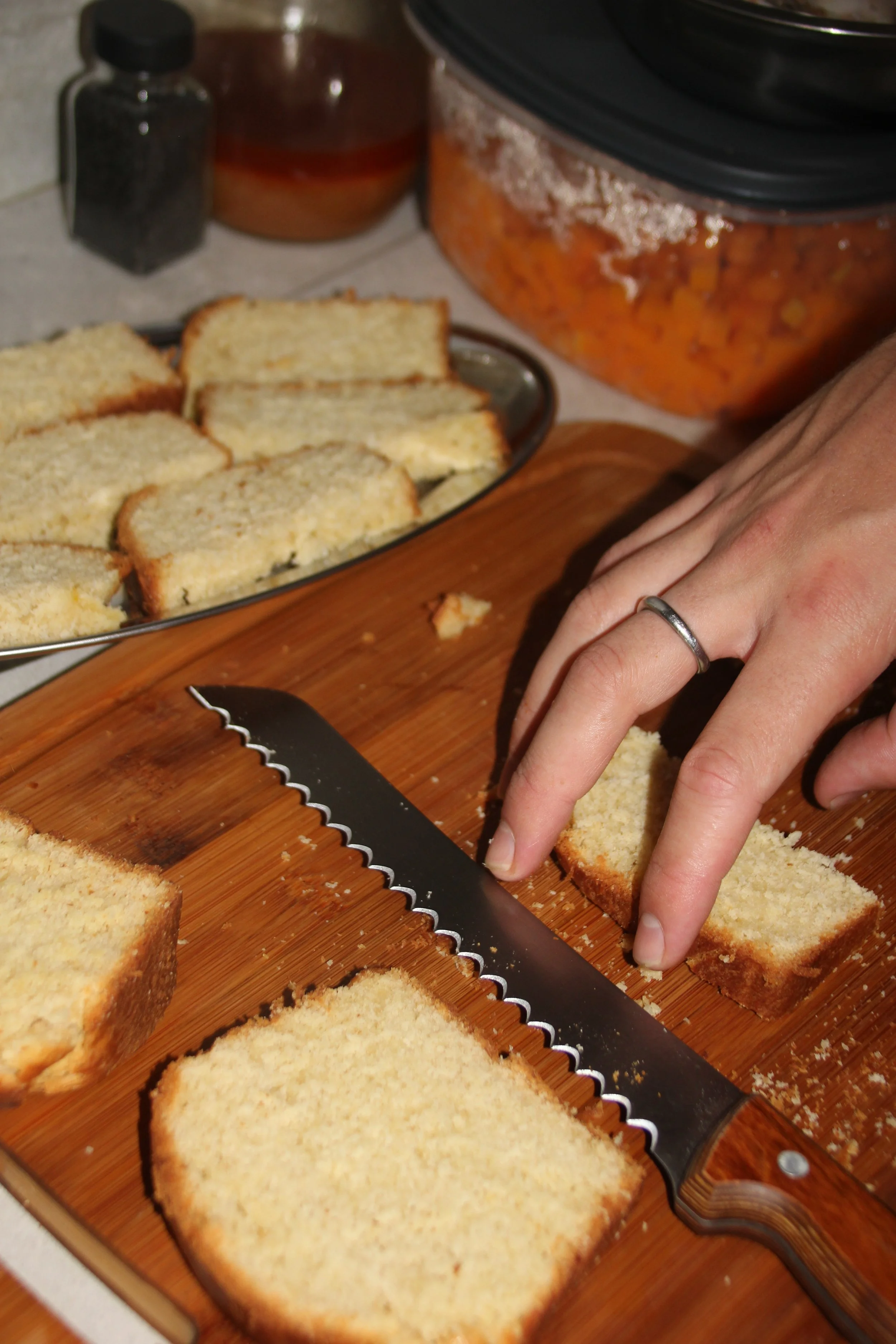 Une personne coupe des tranches de pain de mie avec un couteau dentelé sur une planche en bois, avec une casserole de tarte salée en arrière-plan.