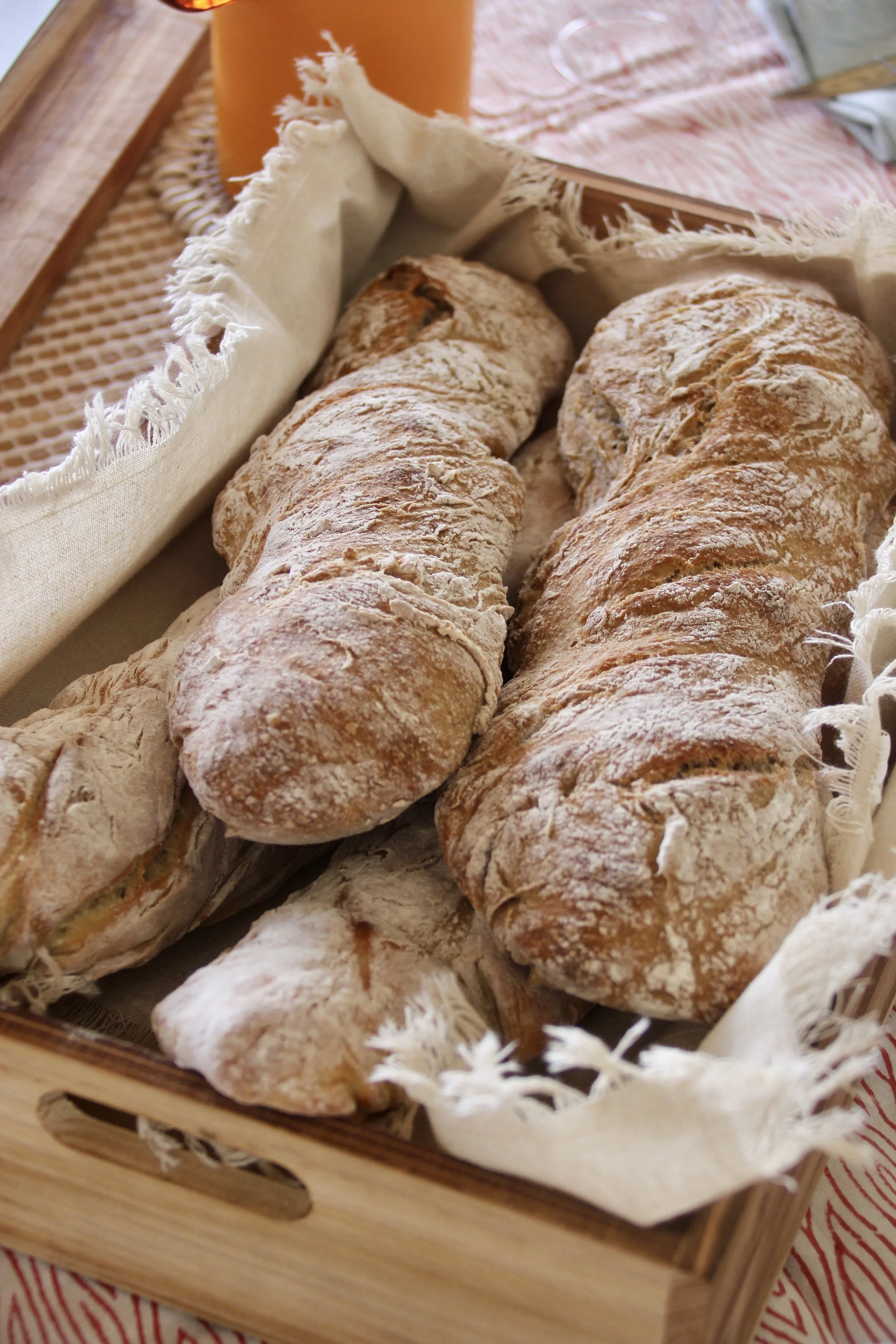 Deux baguettes de pain posées dans une caisse en bois avec un chiffon blanc autour, sur une table avec une nappe à rayures rouges et blanches.
