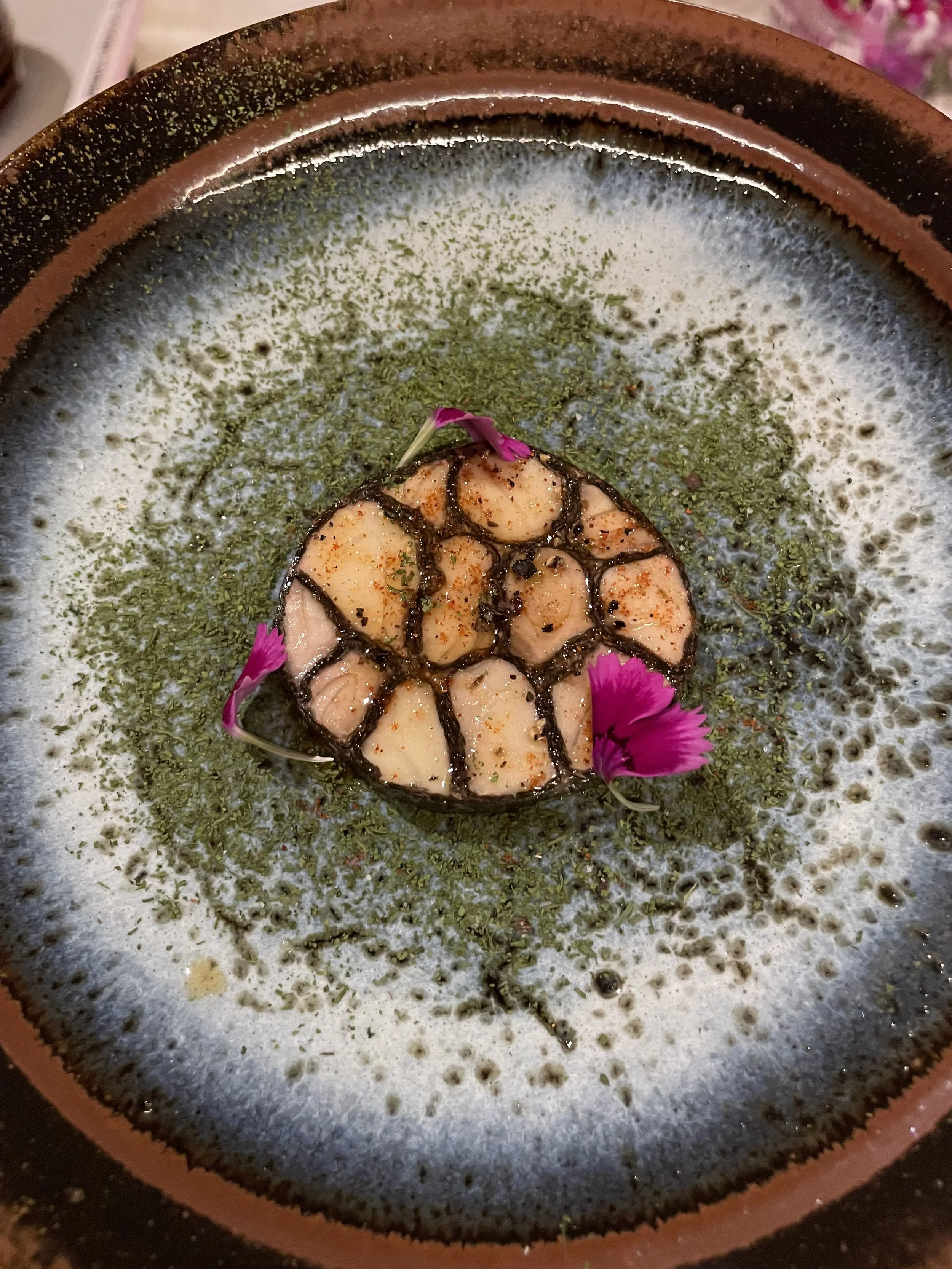 Plat gastronomique avec des crevettes, garnitures vertes et fleurs comestibles roses sur une assiette en céramique