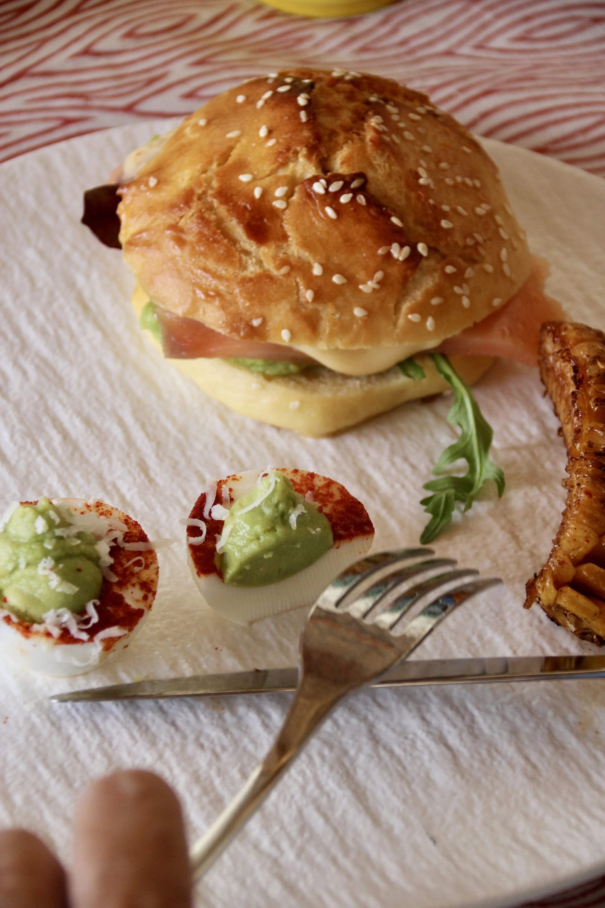 Un sandwich avec un pain brioché, de la viande, de la laitue, du fromage, avec des œufs garnis de guacamole, ainsi que des frites.