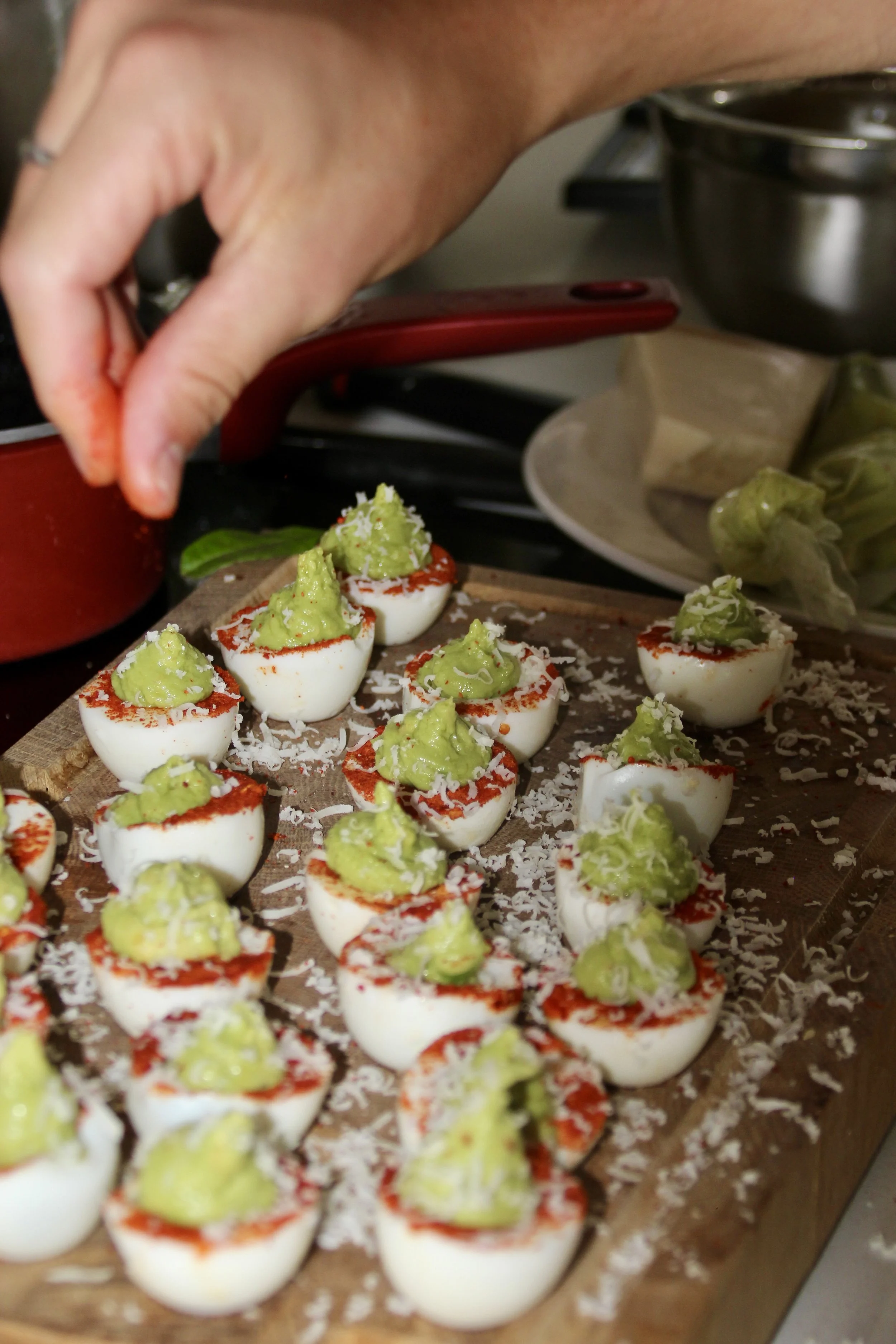 Préparation de bouchées d'œufs devilled garnis d'avocat, sur une planche en bois.