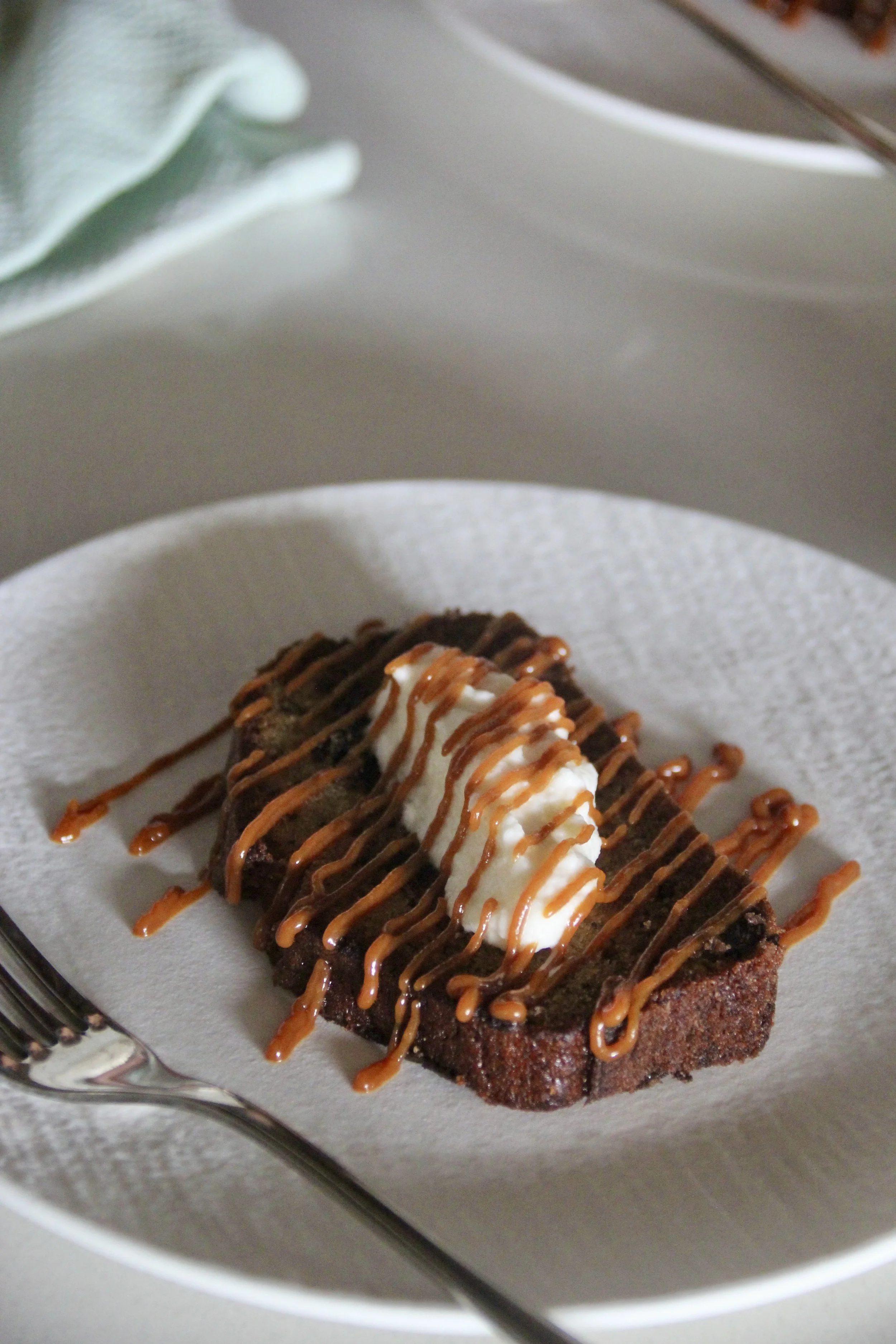 Gâteau au chocolat avec une garniture de crème fouettée et de caramel, servi sur une assiette blanche.