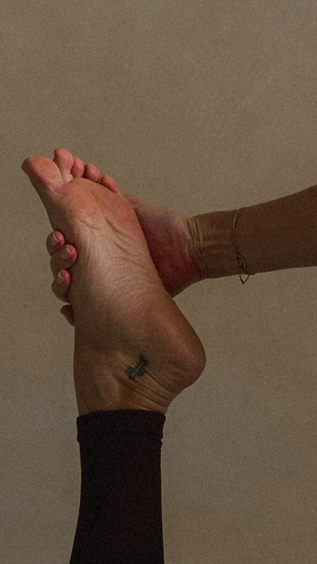 Two hands, one with a tattoo, holding each other against a neutral background.