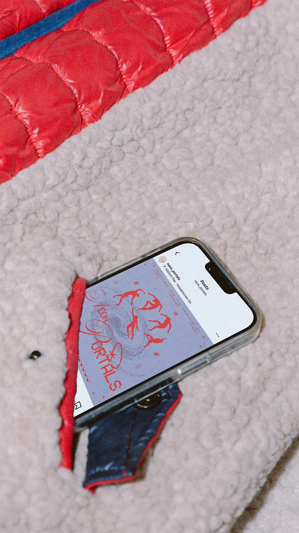 A smartphone sticking out of the pocket of a cream-colored fleece jacket, displaying the Instagram page for a music publication called Neon Portals with vibrant red dancing figures on a blue background.