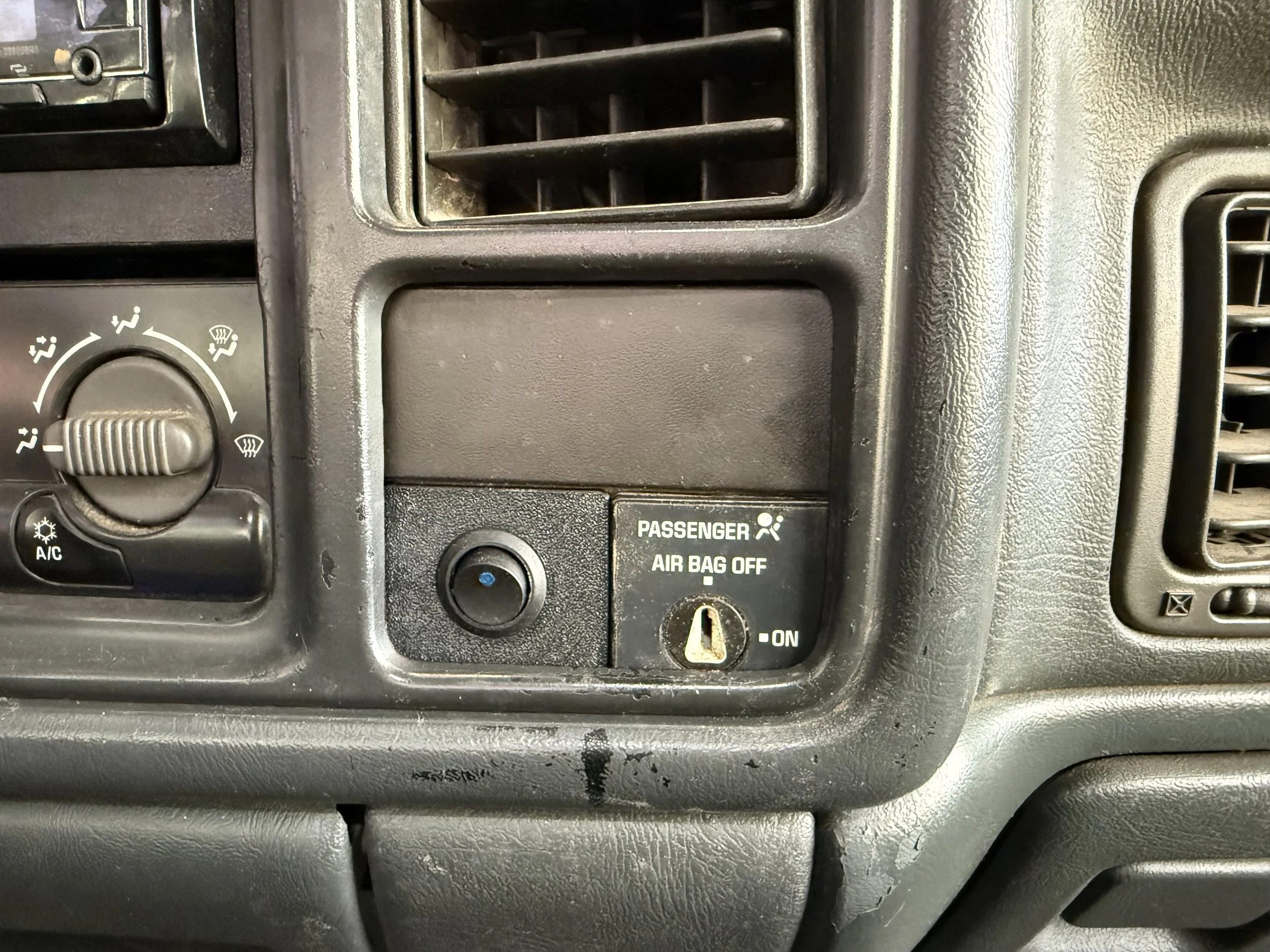 Close-up of a vehicle dashboard showing the air conditioning controls, air vent, and a passenger airbag switch in the off position.
