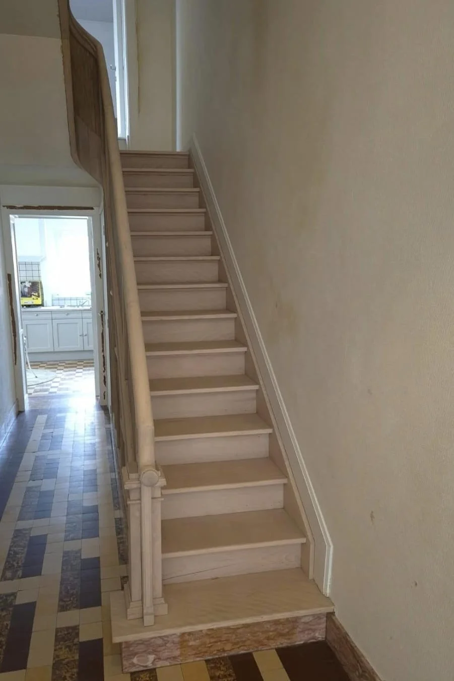 Escalier en bois menant à un étage supérieur, avec une rampe en bois et mur beige