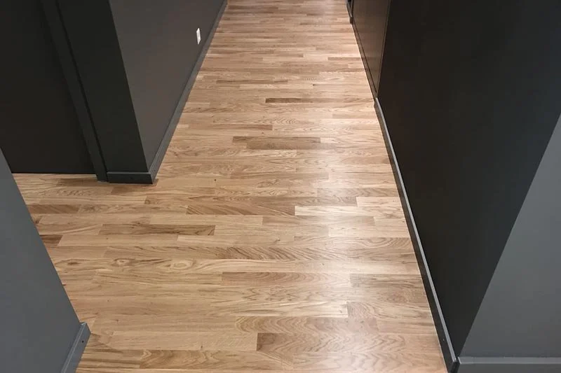 Plancher en bois clair dans un couloir intérieur avec des murs gris foncé et des portes en bois foncé.