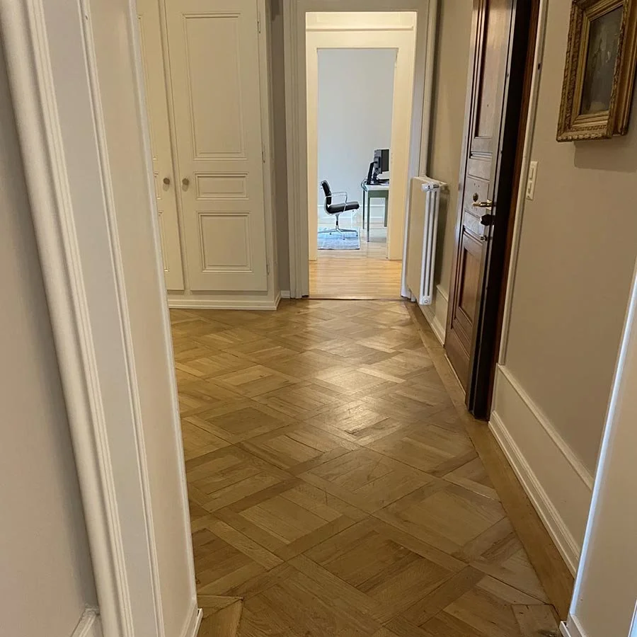 Vue d'un couloir intérieur menant à un bureau avec un fauteuil et un ordinateur.