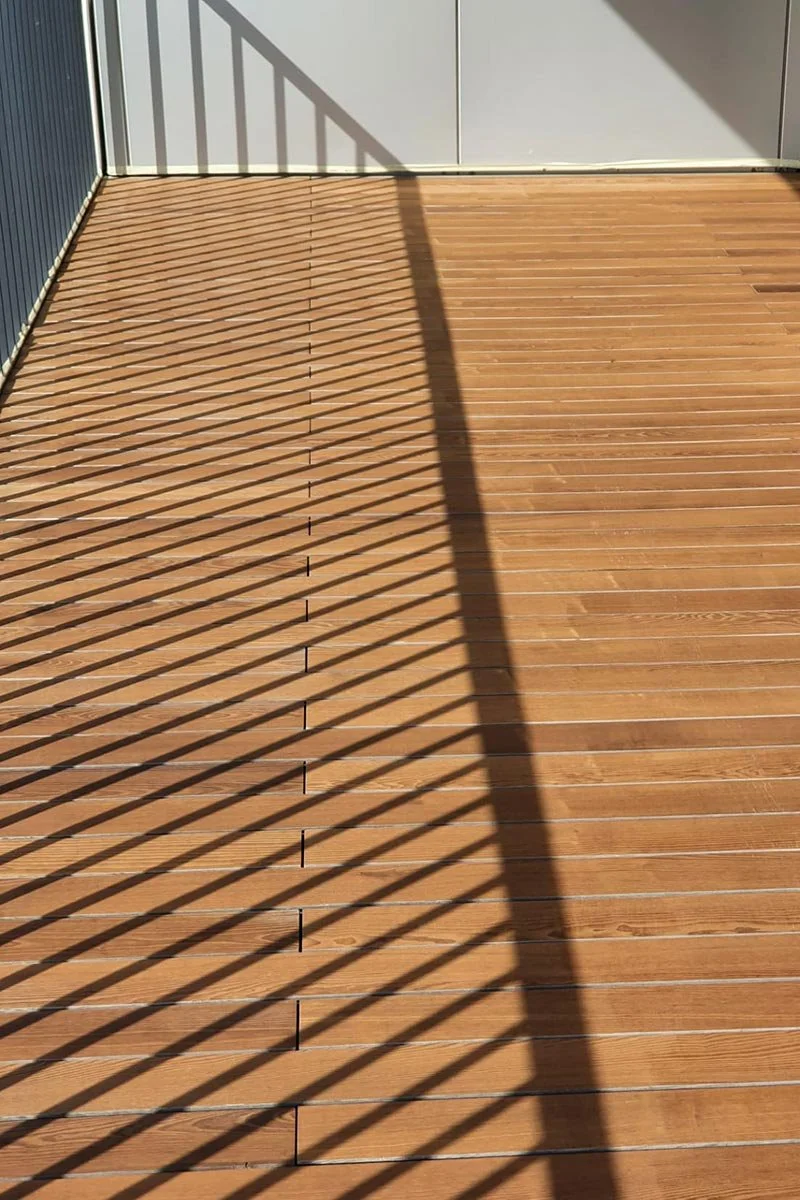 Rampe en métal avec ombres linéaires projetées sur un sol en bois.