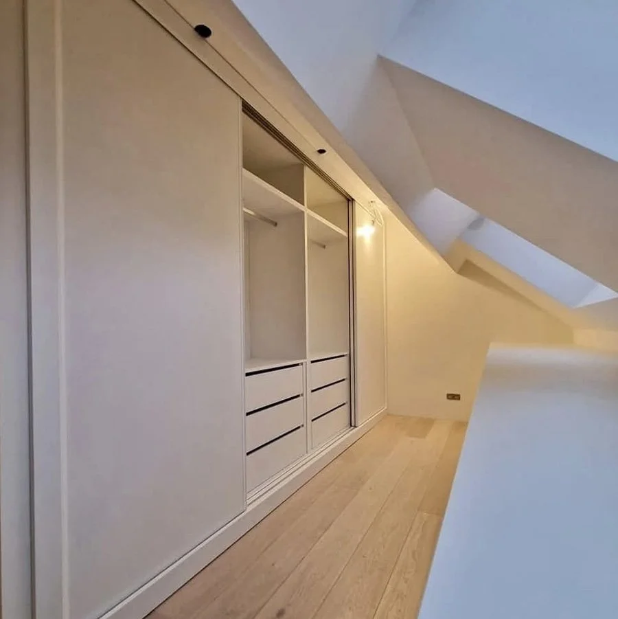 Placard blanc dans une pièce mansardée avec lambris en bois clair.