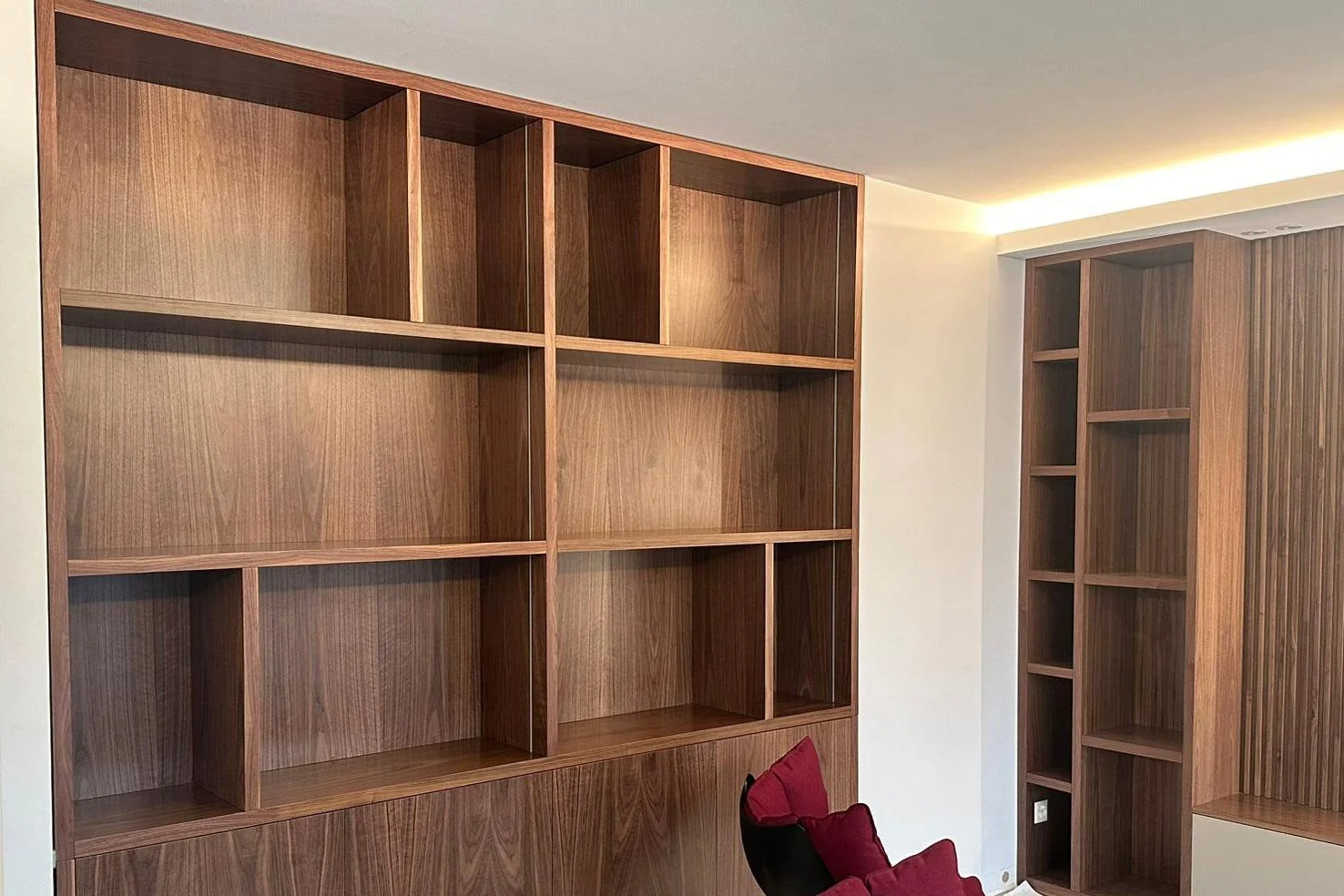 Meubles en bois avec plusieurs étagères vides dans une pièce, une chaise noire avec un coussin rouge est partiellement visible