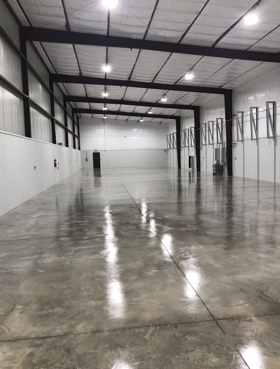 Empty, spacious indoor warehouse with polished concrete floor and high ceiling with bright overhead lights.