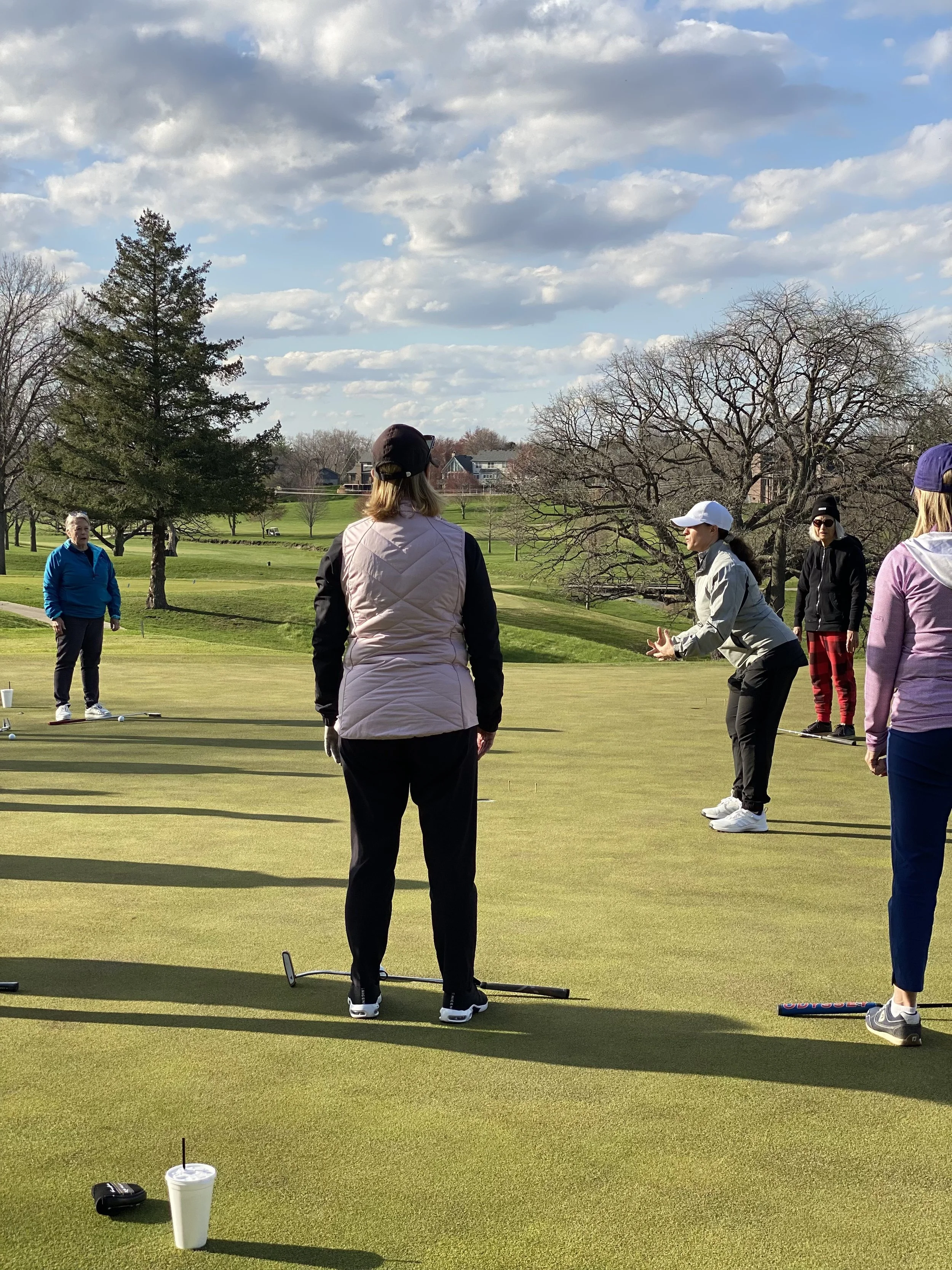 Group of golfers on a green practicing putting outdoors on a sunny day.