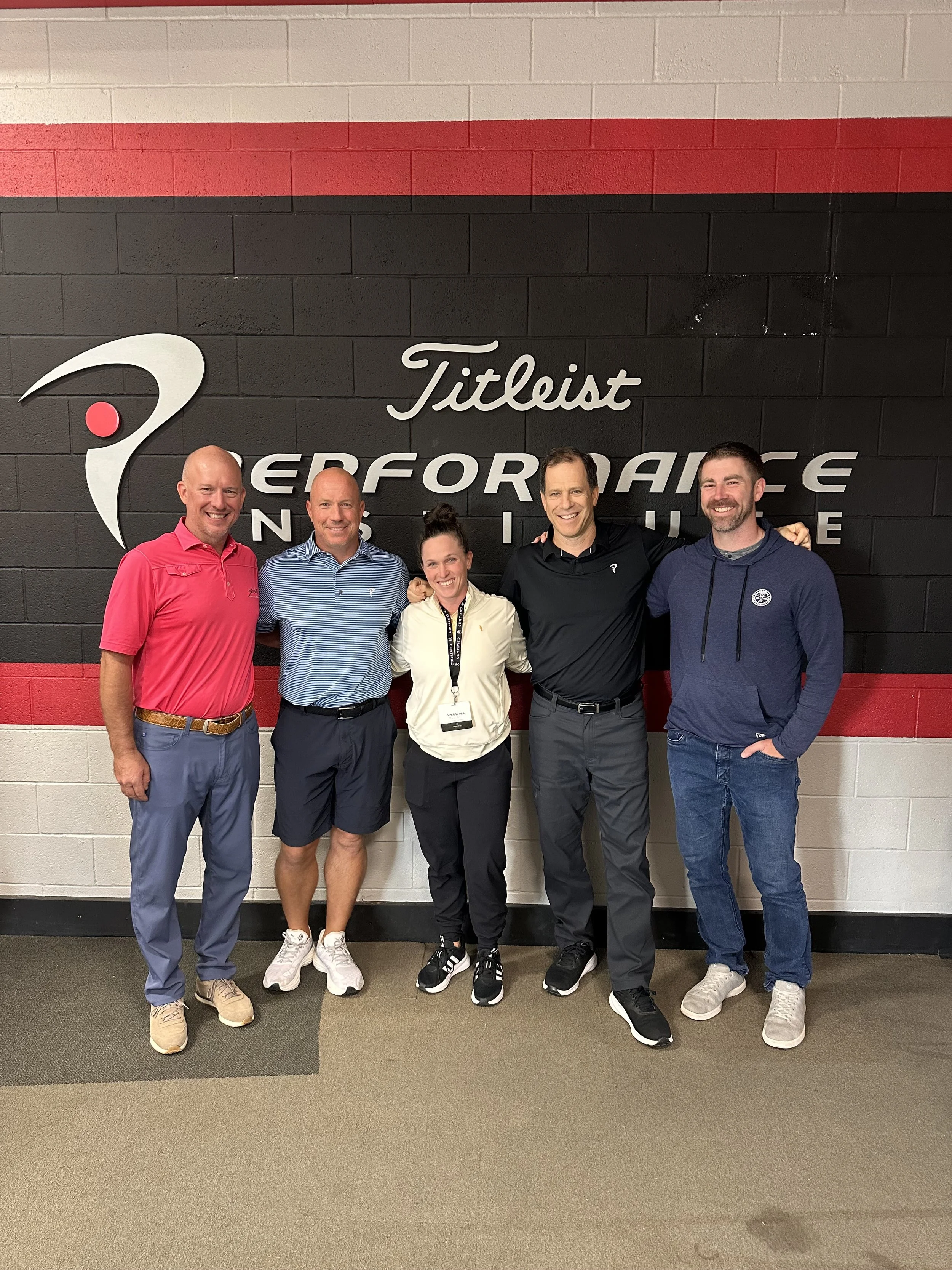 Five people standing in front of a wall with the Titleist Performance Institute logo, smiling and posing for a group photo.