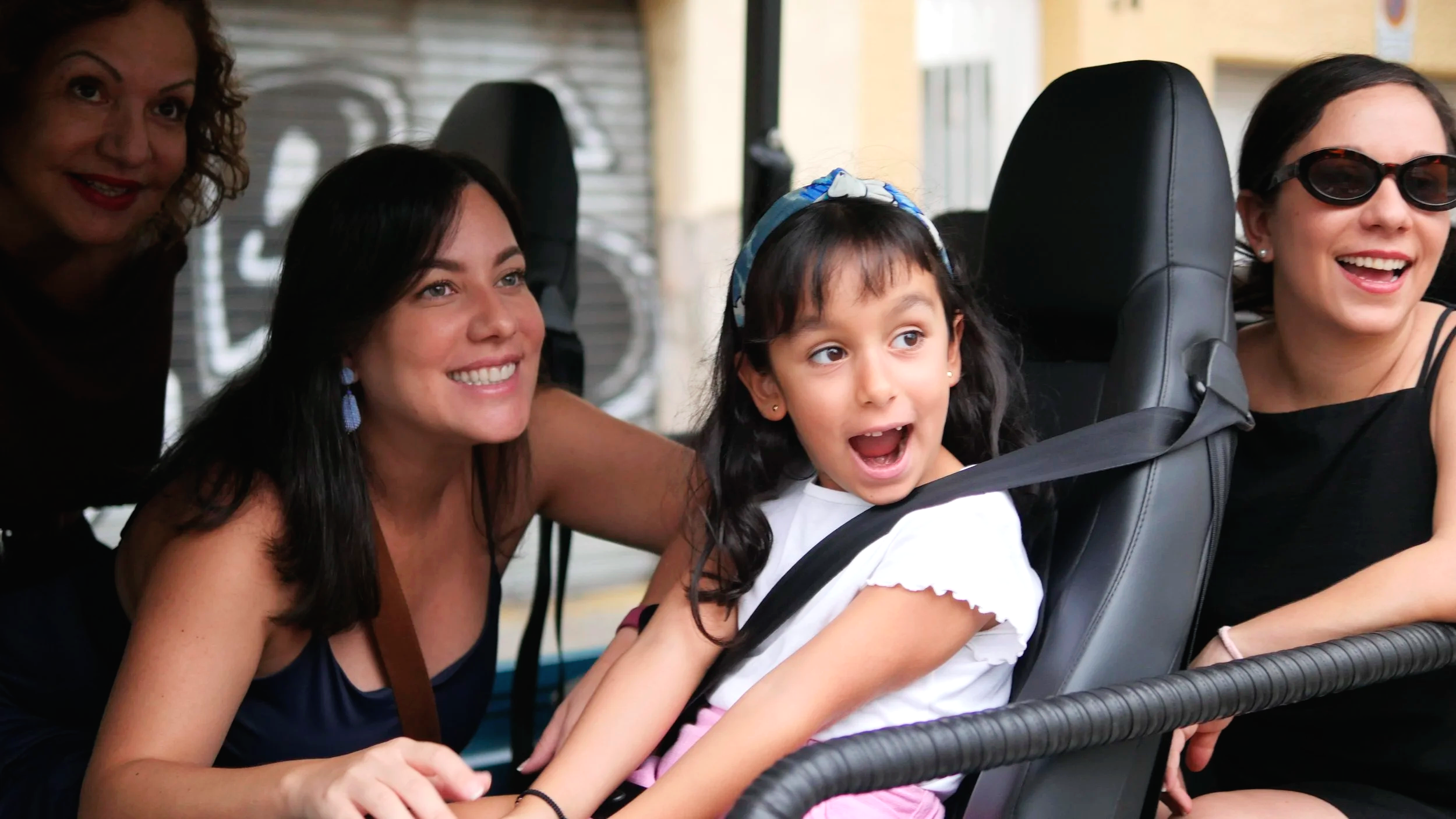 Four women and a young girl in a vehicle, smiling and enjoying their time together.
