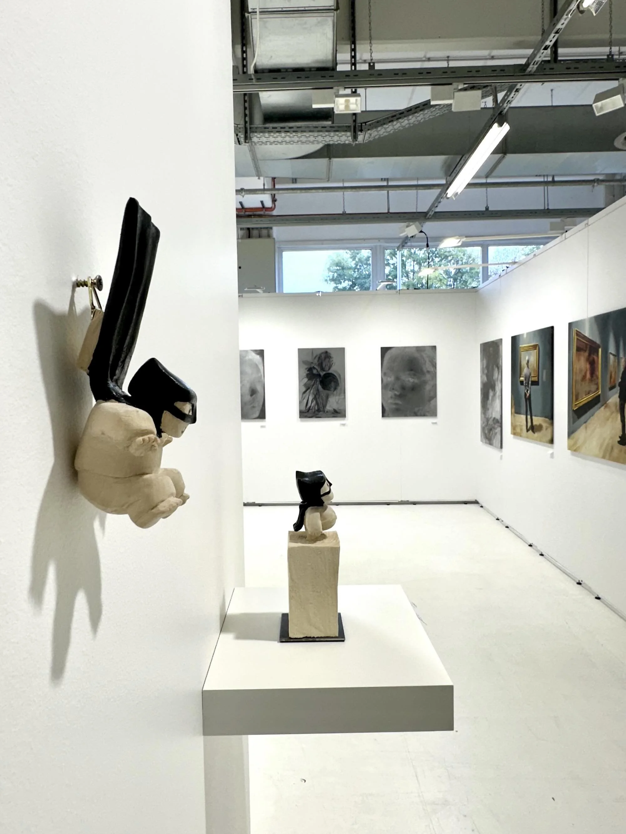 Kunstgalerie mit Skulpturen und Gemälden an weißen Wänden, helles Deckenlicht, Fenster mit Blick nach draußen.