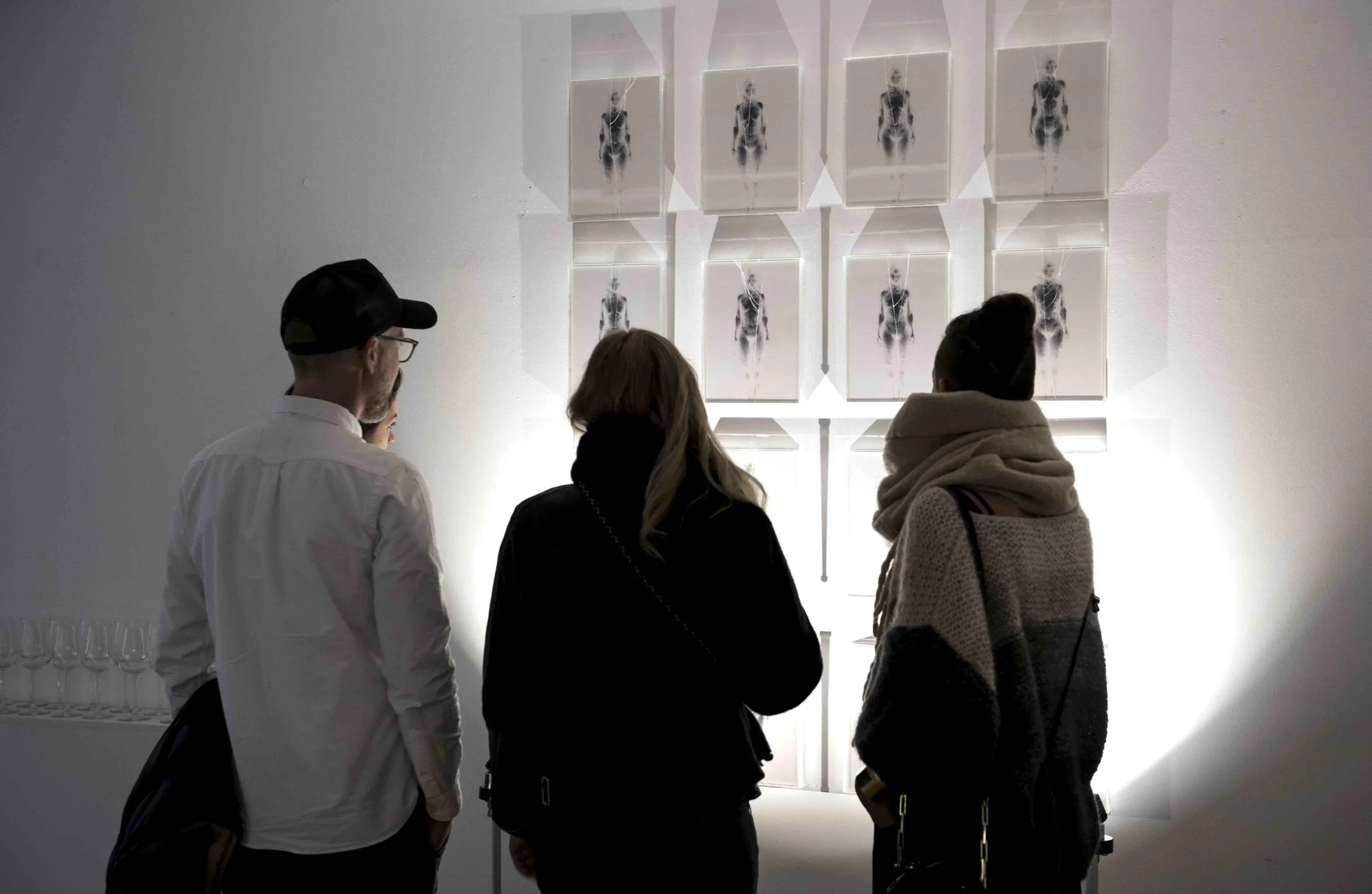 Drei Menschen betrachten eine Wand mit mehreren Röntgenbildern von menschlichen Skeletten in einem Kunstmuseum.