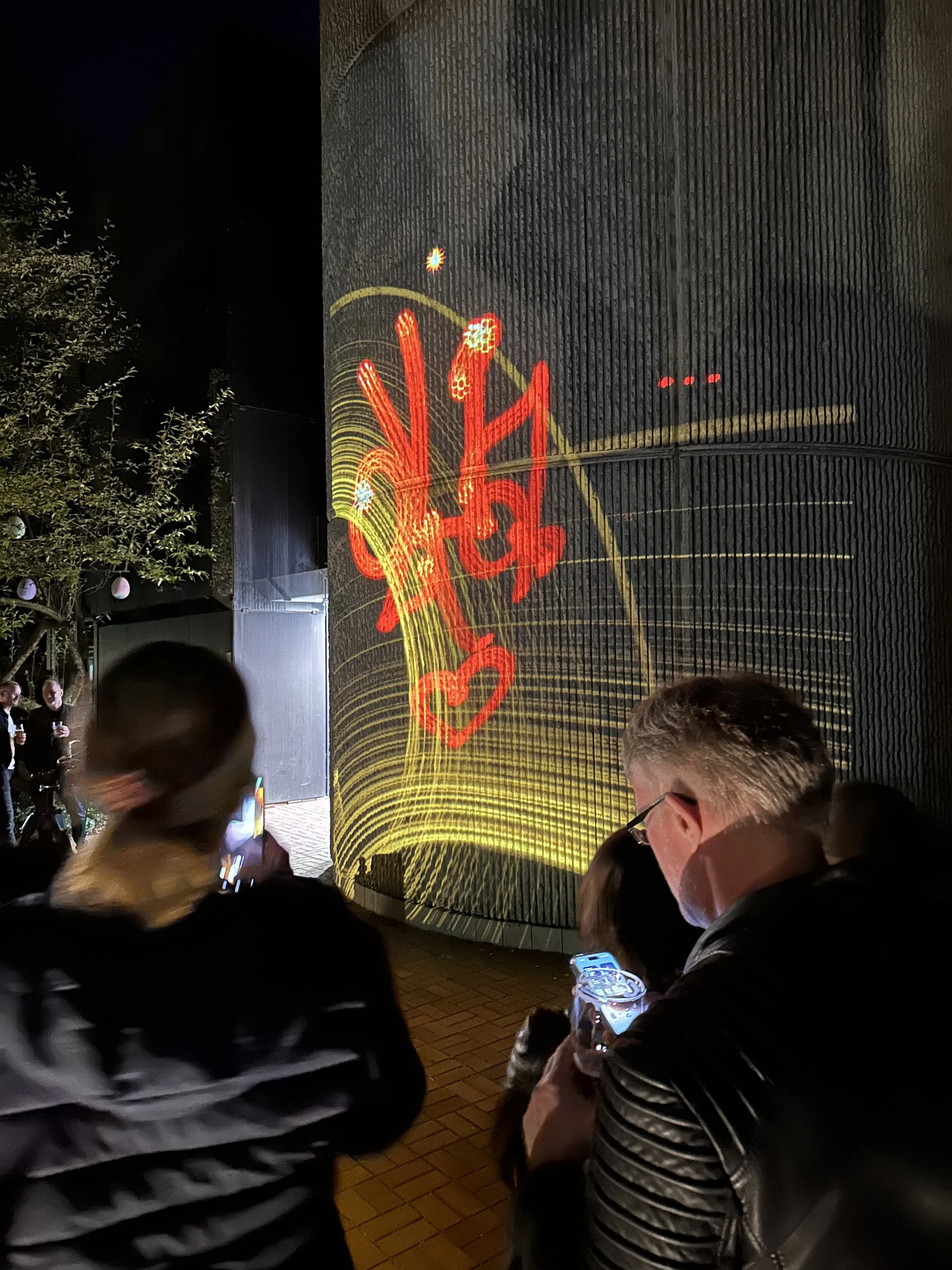 Menschen versammeln sich vor einer Wand mit einem hell leuchtenden, künstlerischen Graffiti, das mit roten und gelben Lichtern gestaltet wurde.