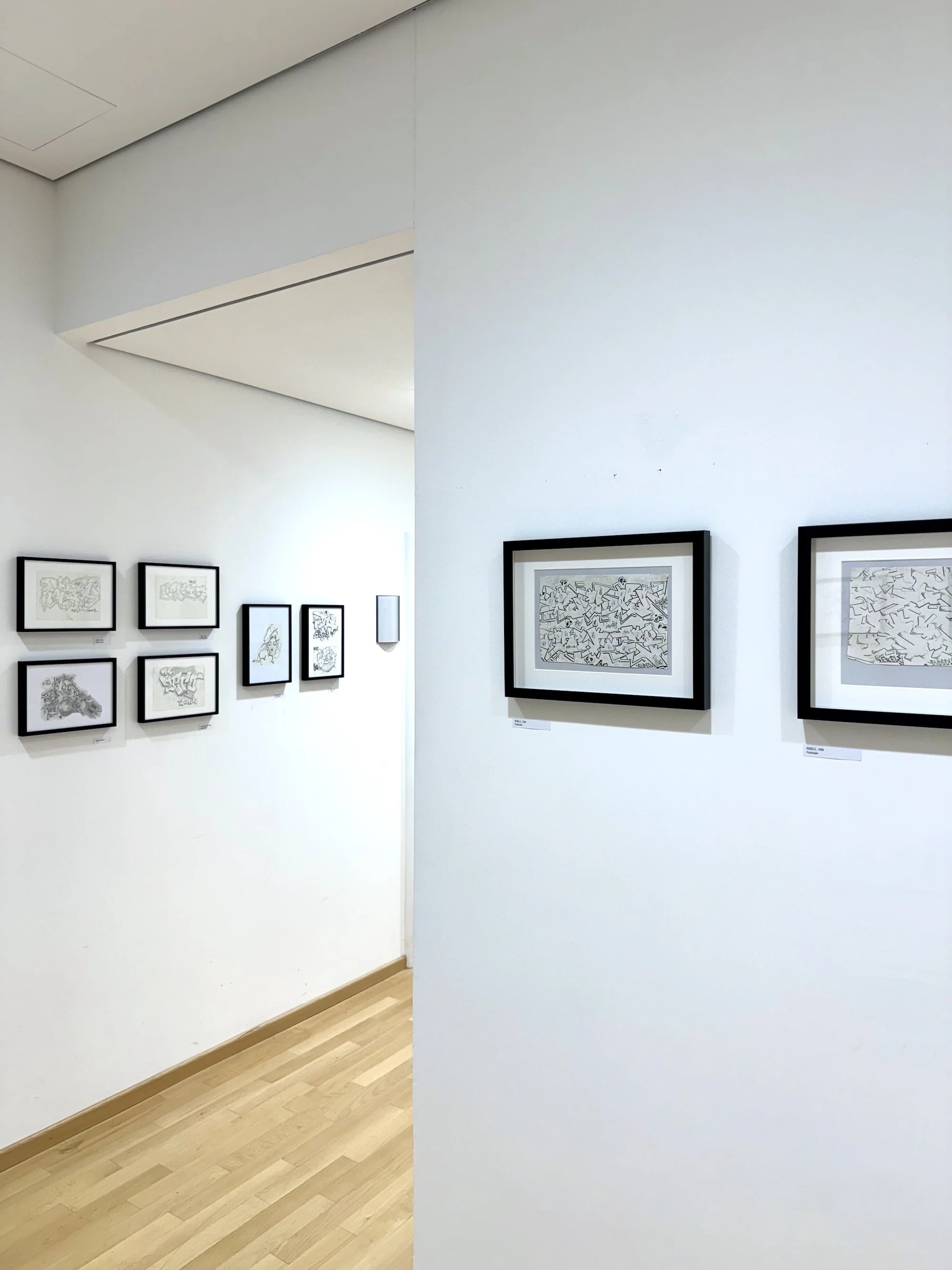 Bilder in einem Kunstmuseum mit schwarzen Rahmen an weißen Wänden, die abstrakte Skizzen oder Zeichnungen zeigen.