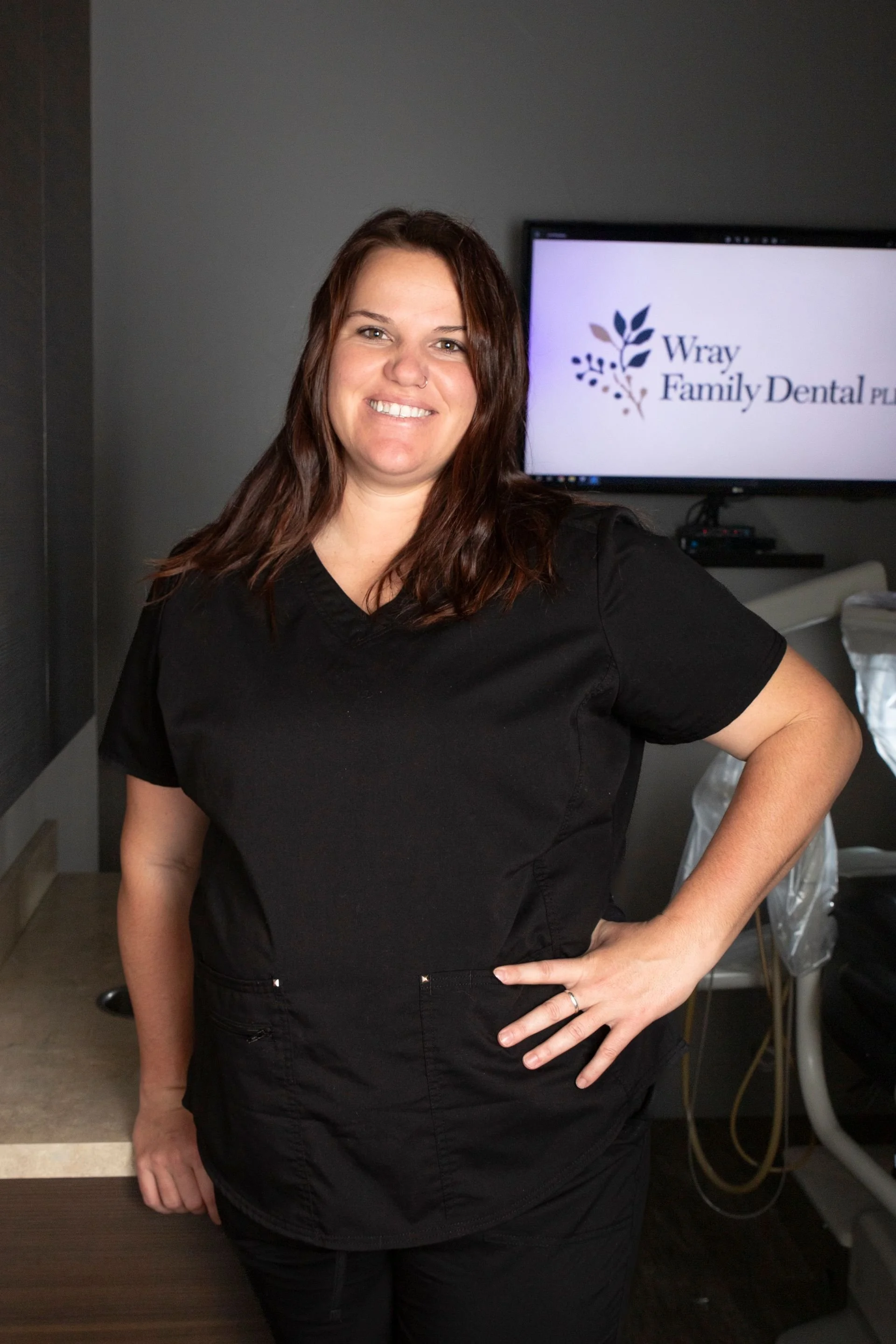 A woman in black scrubs smiling in a dental office