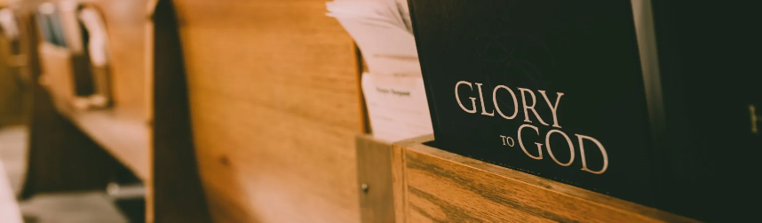 A book titled 'Glory to God' on a wooden church pew next to religious papers.