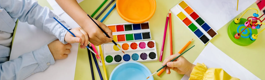 Children's hands painting with watercolor paints on a table with art supplies